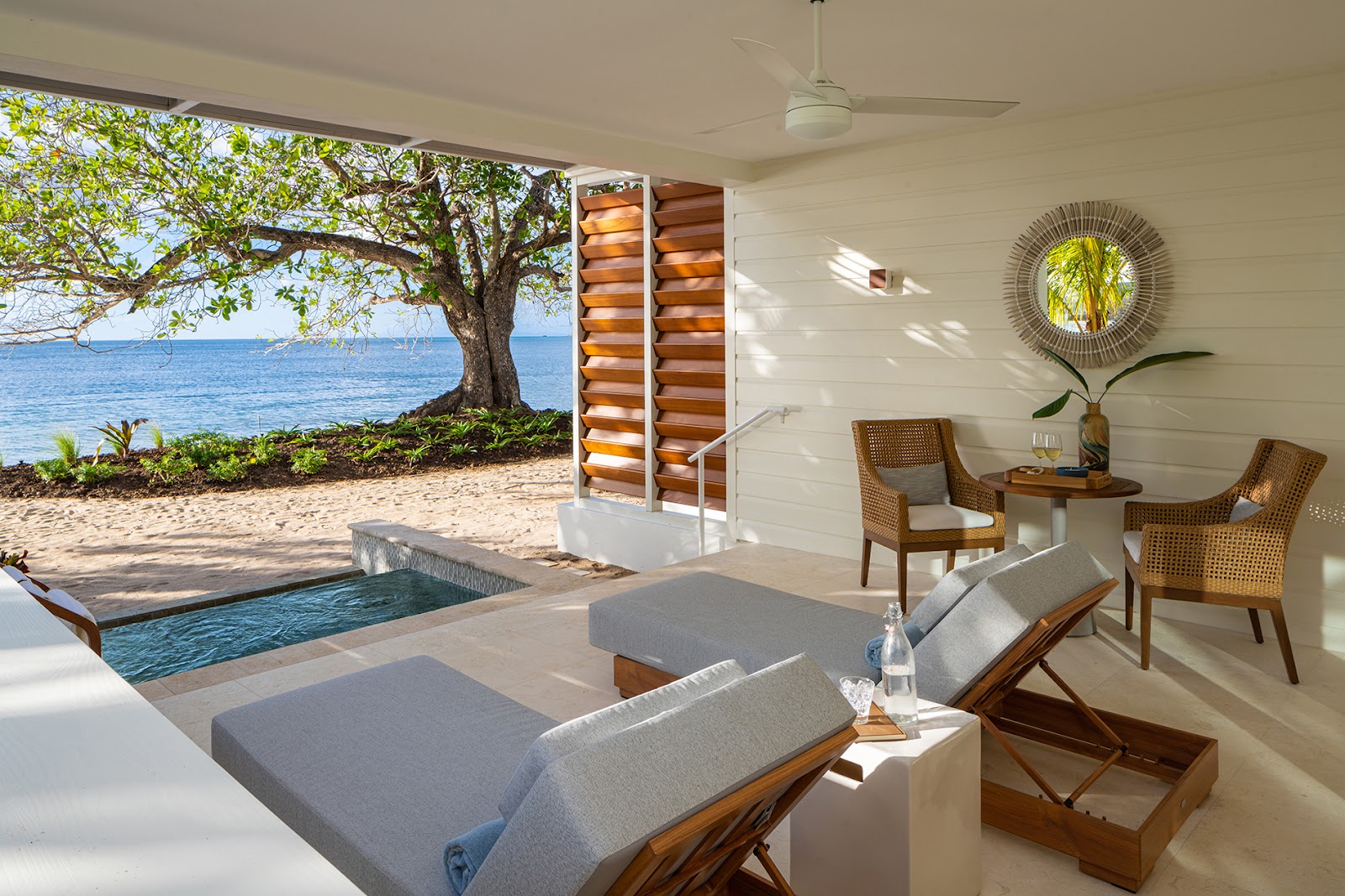 Beachfront suite at Sandals Halcyon Beach with loungers, private plunge pool, ocean view, and large tree on sandy shore.