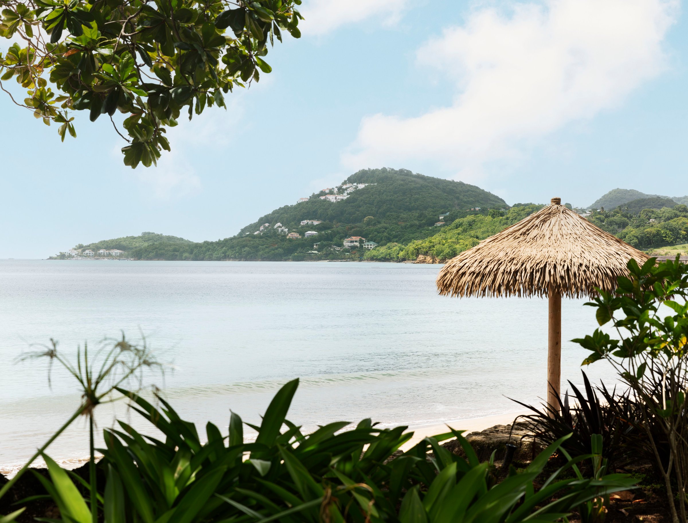 Thatched beach umbrella among tropical plants looking across the bay.