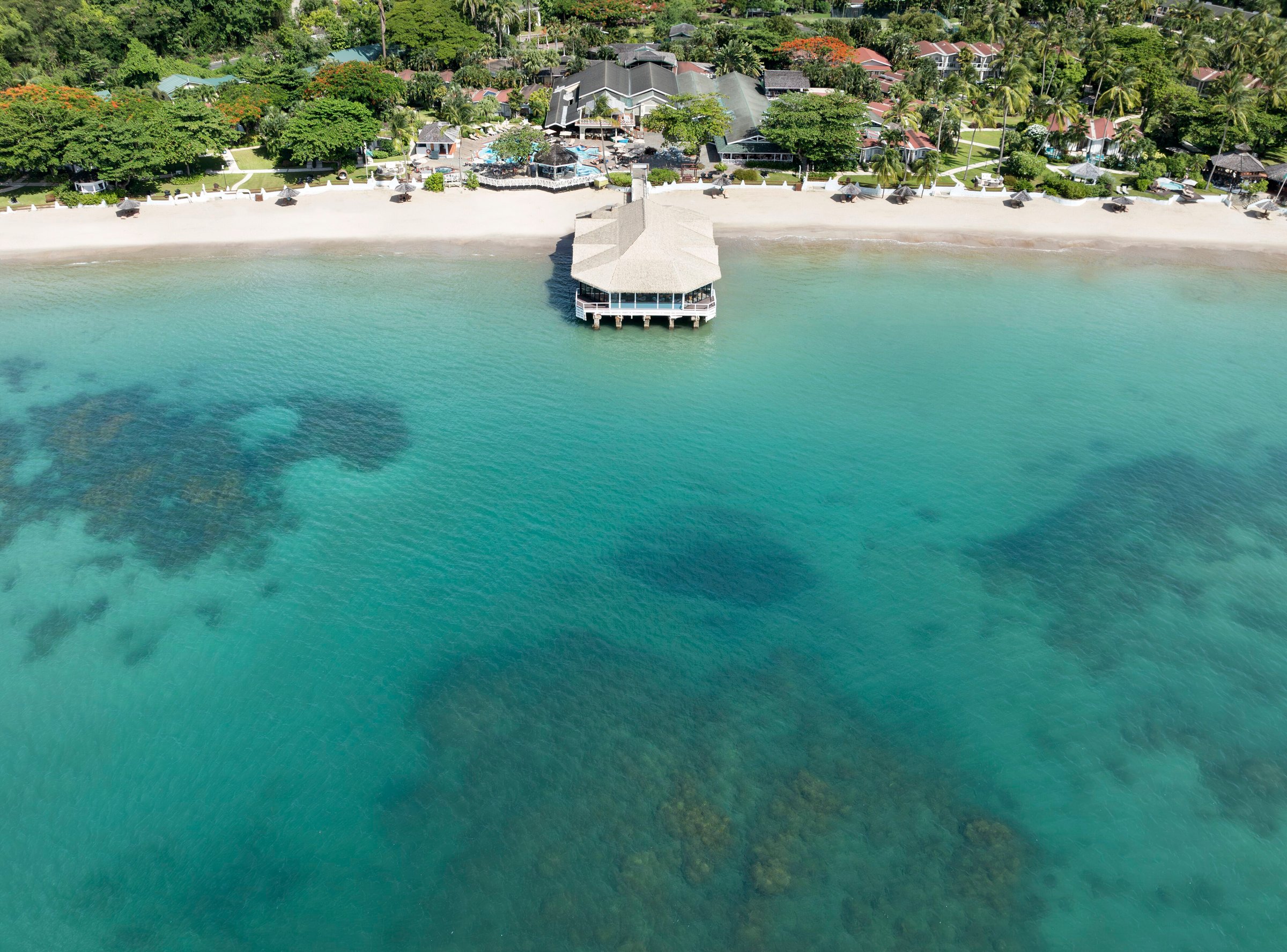 Aerial of Kelly's Dockside over-water restaurant above clear reef-dotted water.