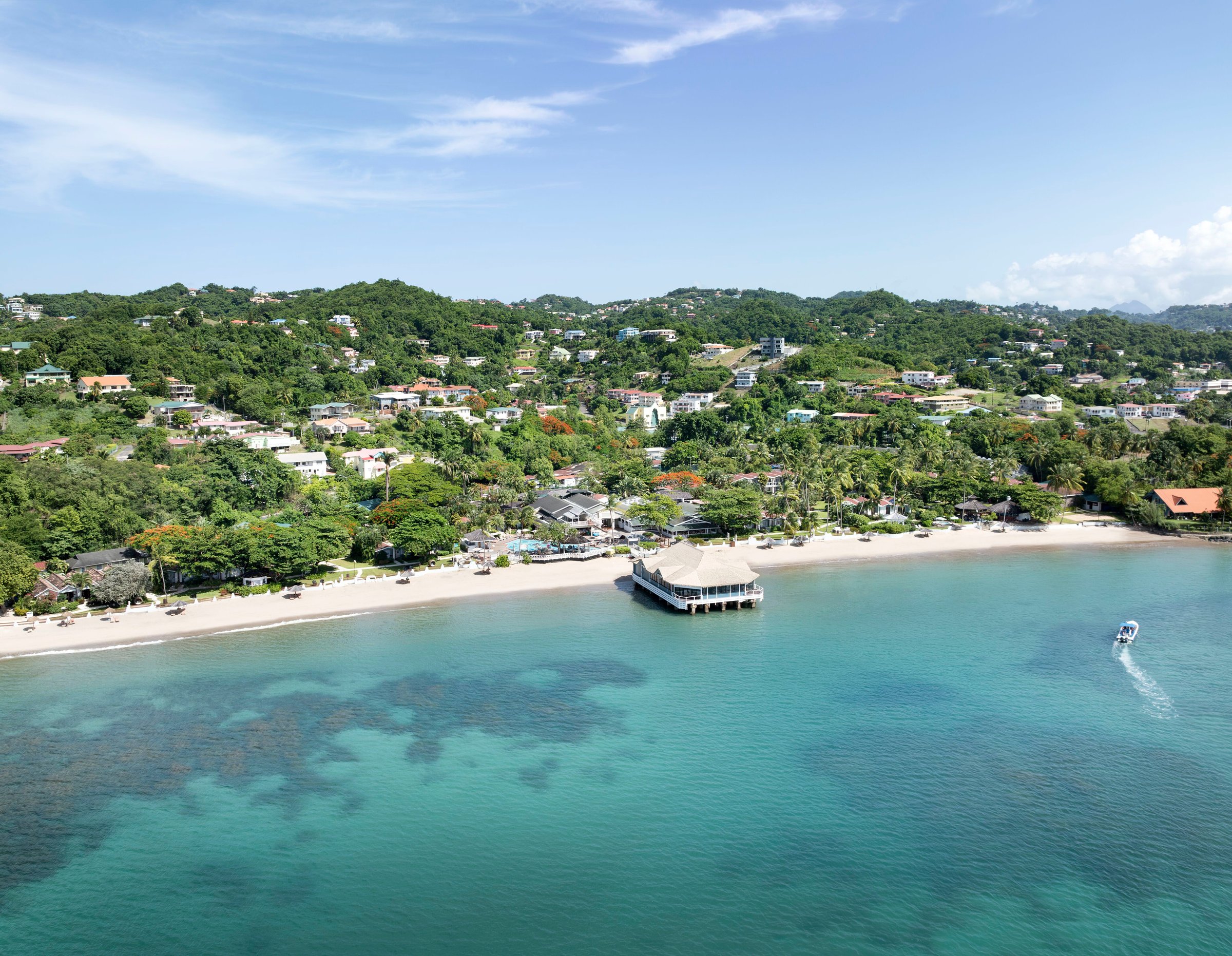Aerial over the bay to the beach, Kelly's Dockside pier and green hills.