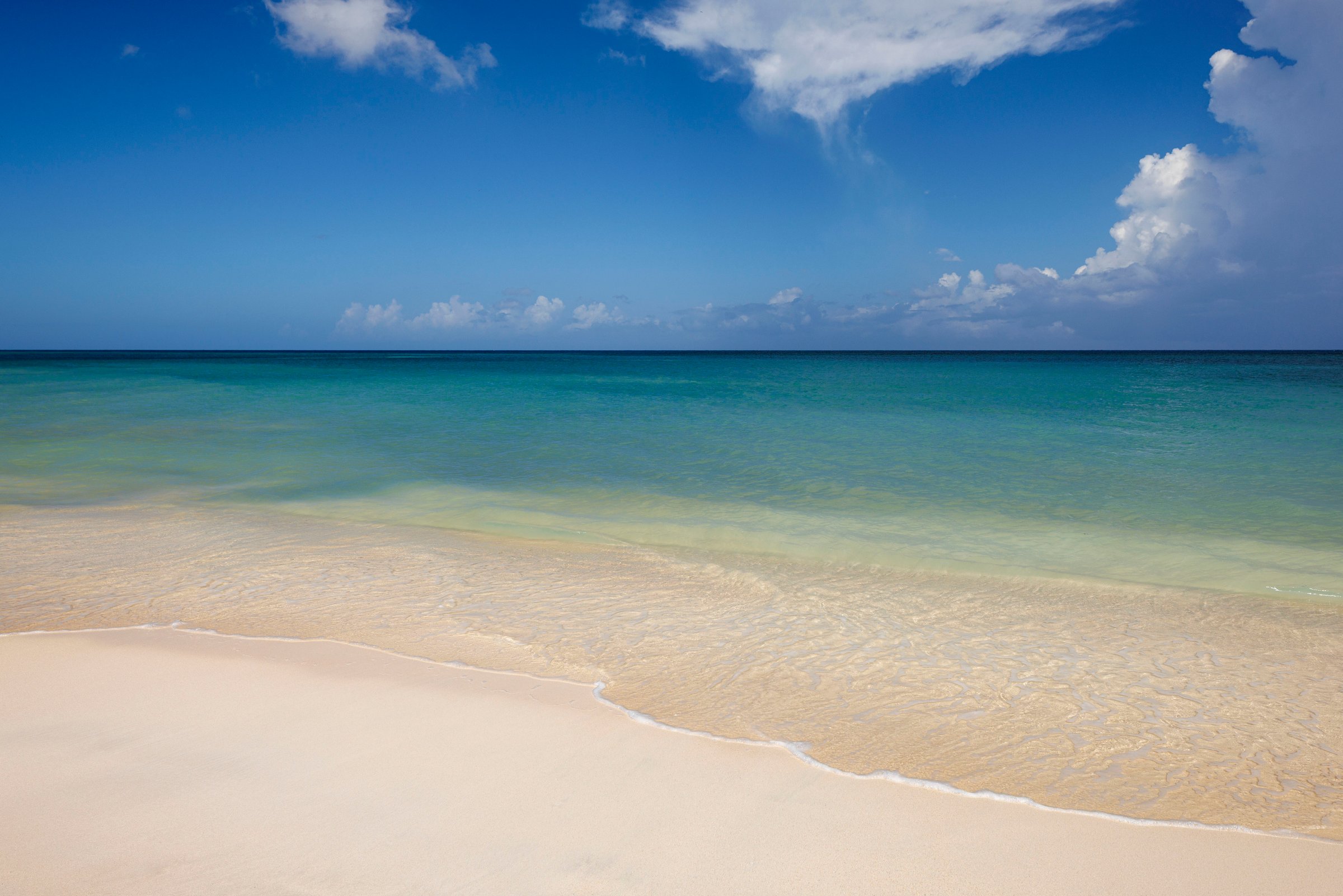 Calm turquoise water lapping the pale sand beach under a blue sky.