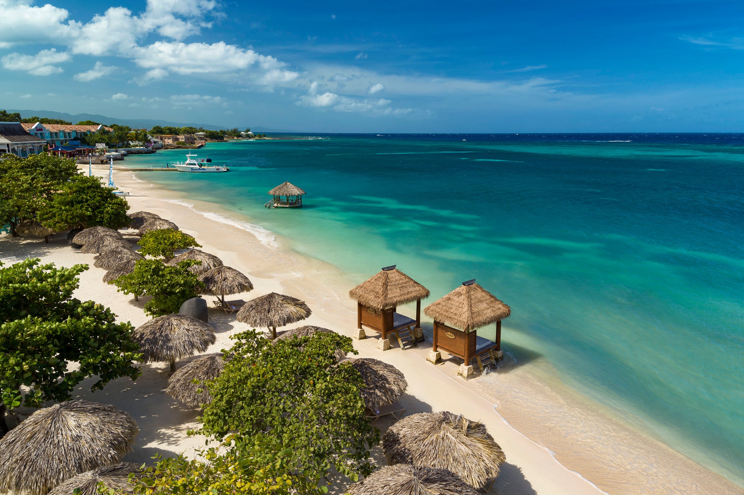 Beachfront cabanas and thatched umbrellas along the turquoise water.