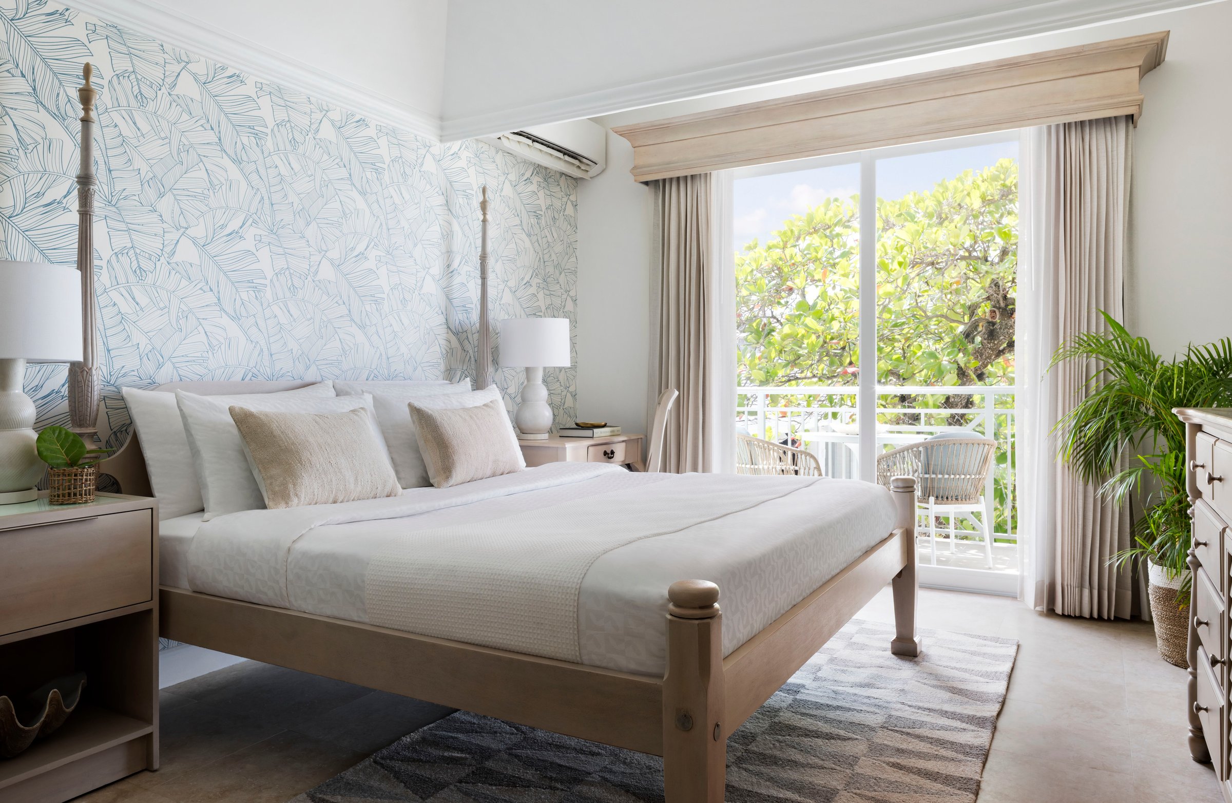 Bright bedroom with a four-poster bed, leaf wallpaper and balcony doors.