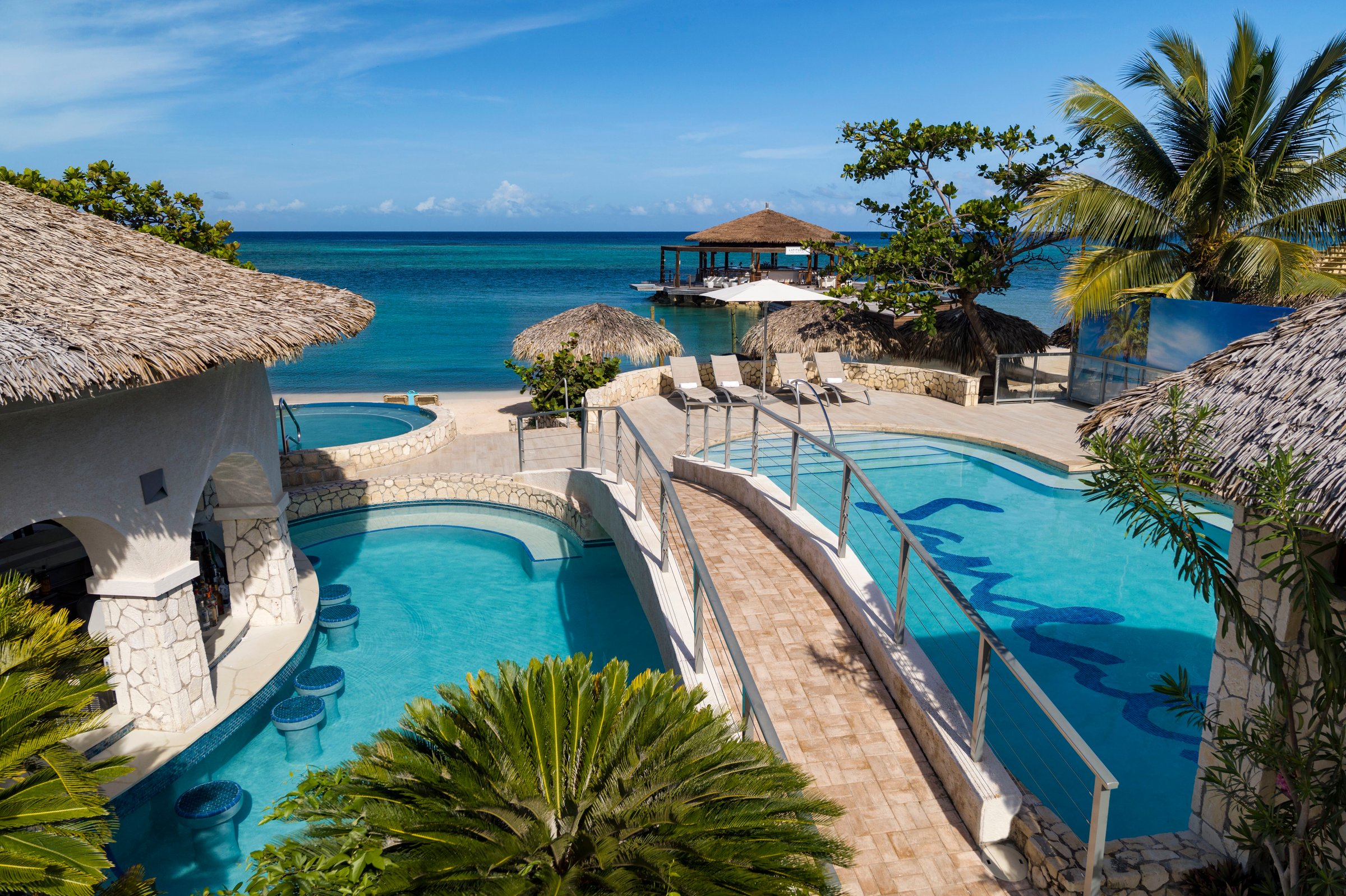 Pool with a footbridge and swim-up stools beside the beach and an overwater gazebo.