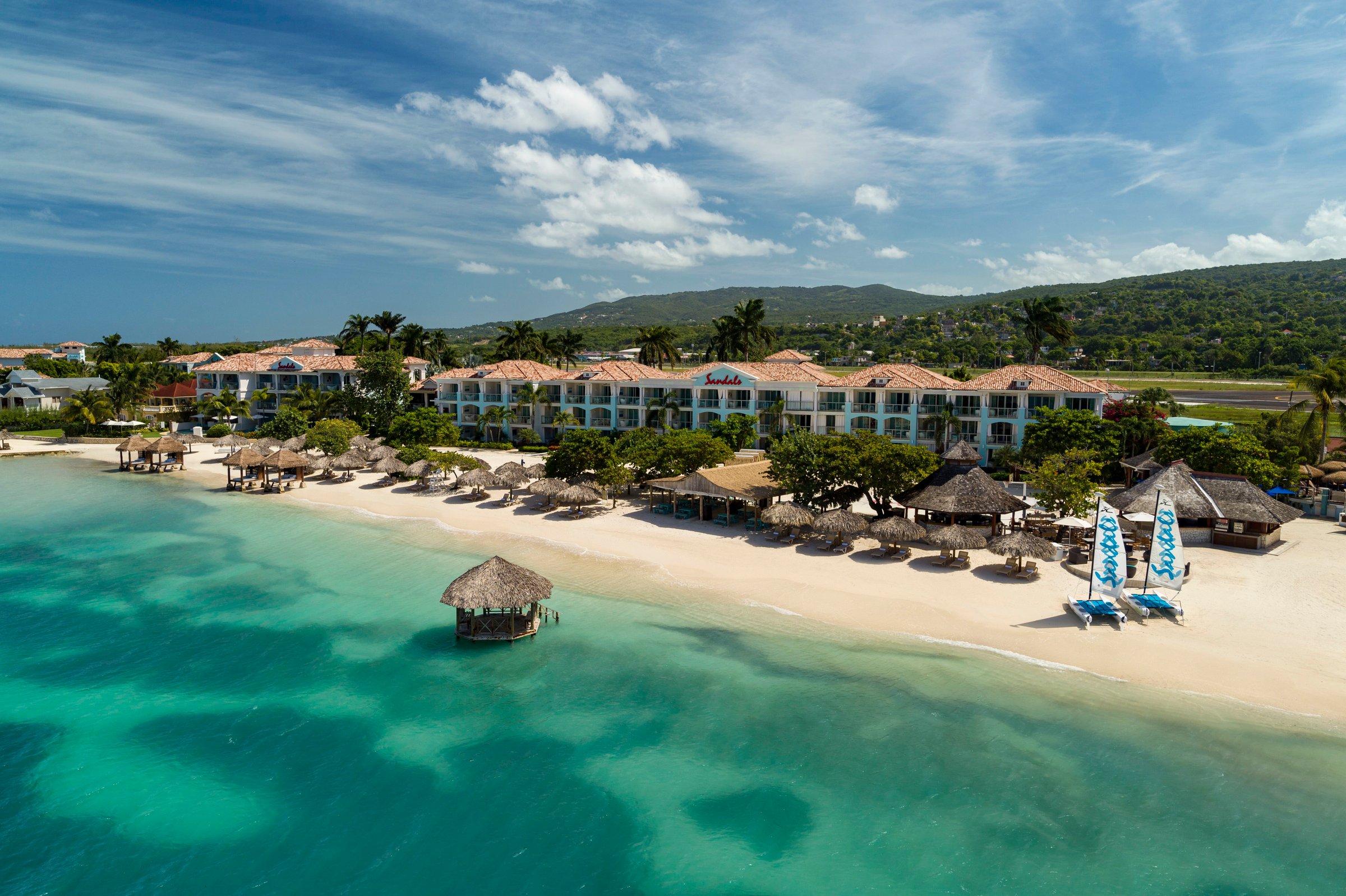 Aerial of the whole resort on its beach with the overwater gazebo and the hills behind.