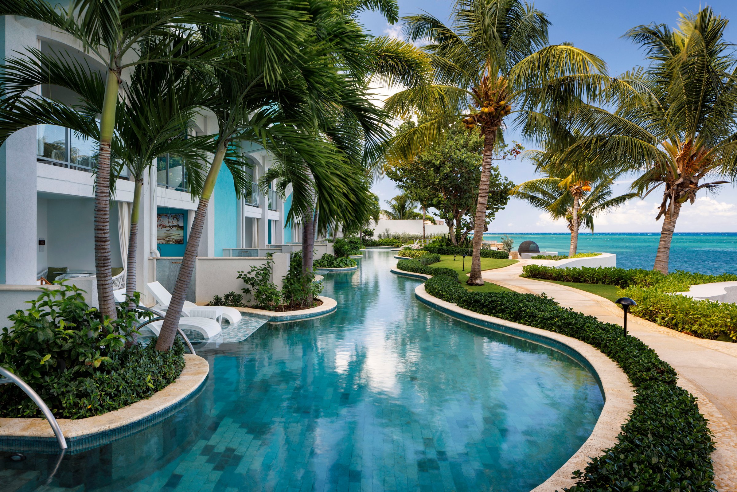 Winding swim-up suite river pool through palms toward the sea.