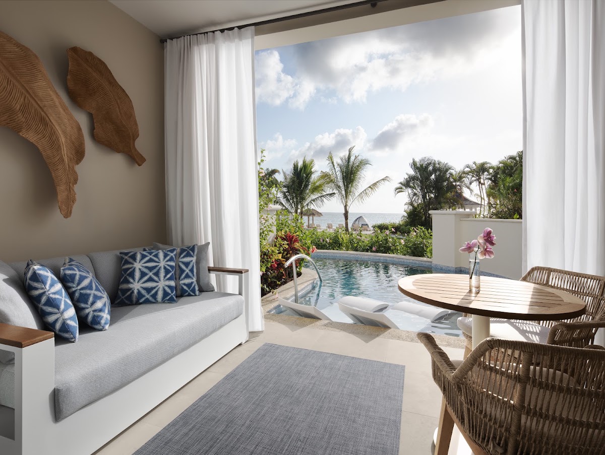 A beachfront suite at Sandals Negril features a private infinity pool, outdoor seating, and ocean views framed by palm trees and white curtains.