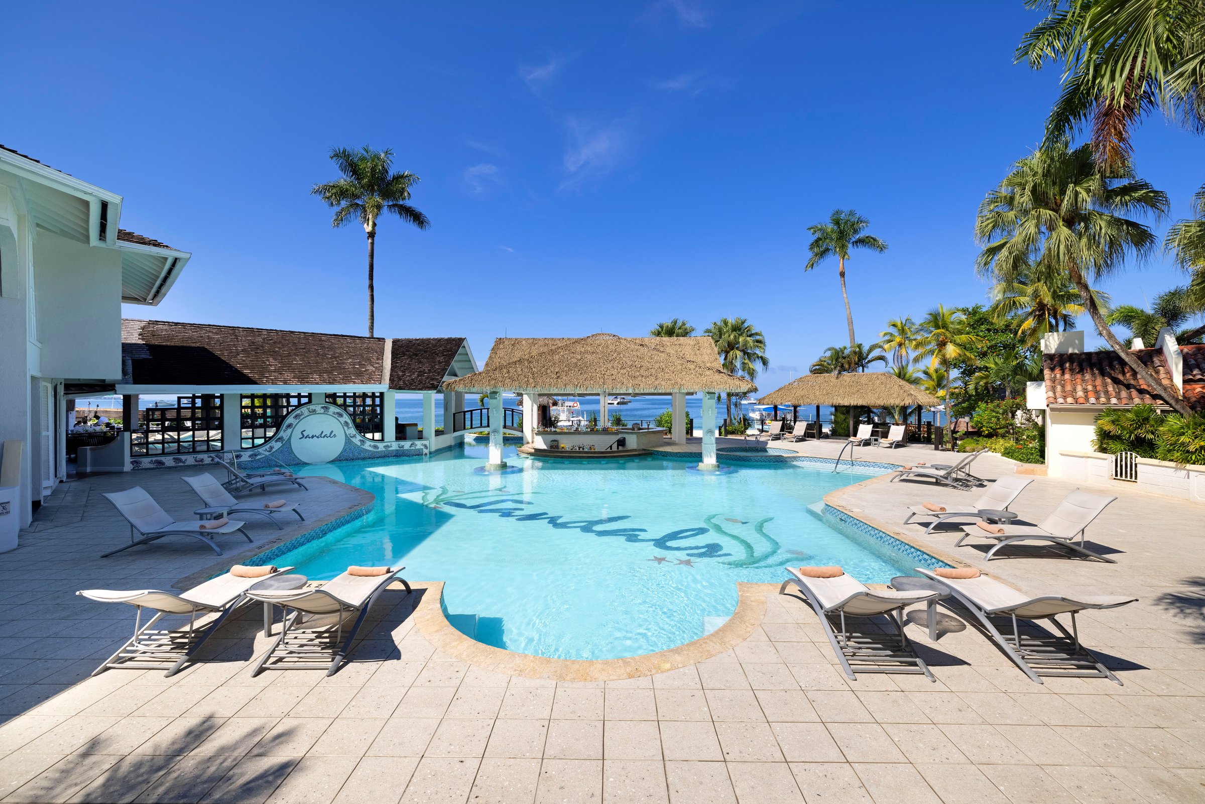 Main pool with the Sandals mosaic, loungers and a thatched swim-up bar.