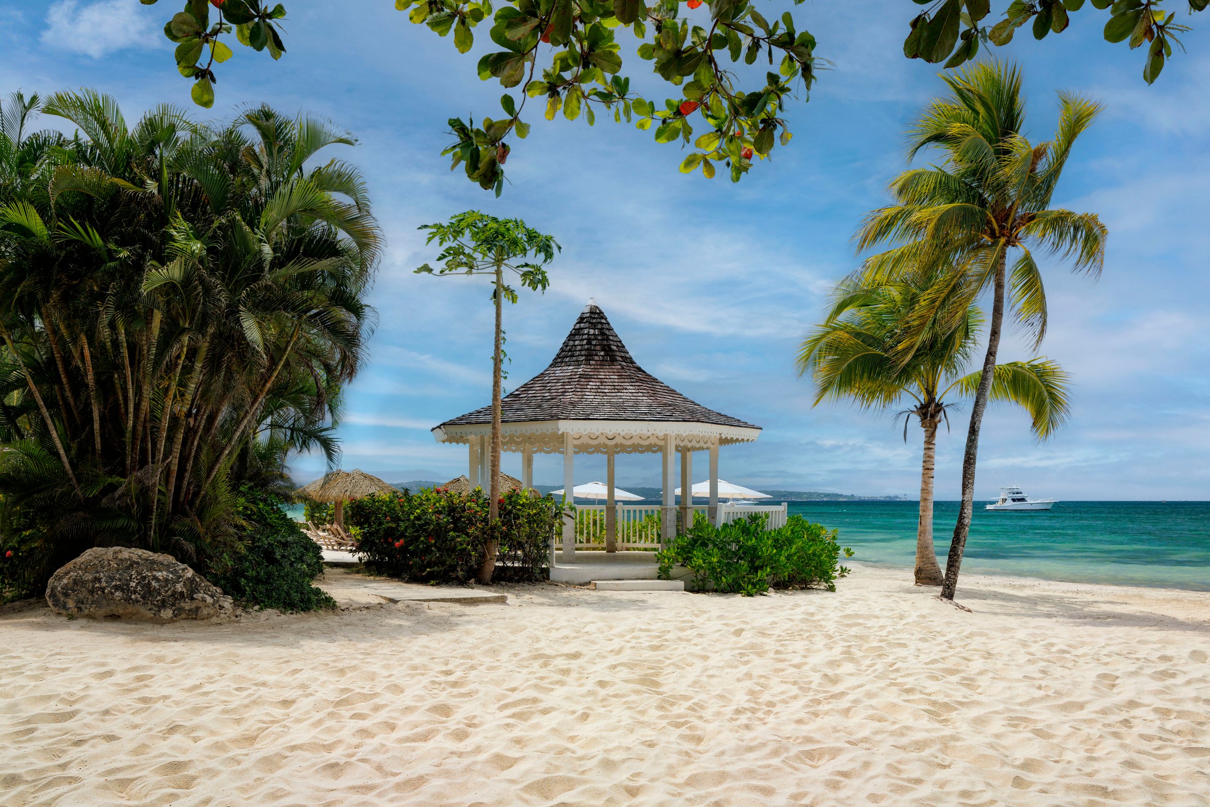 Thatched beach gazebo framed by palms on the white sand.
