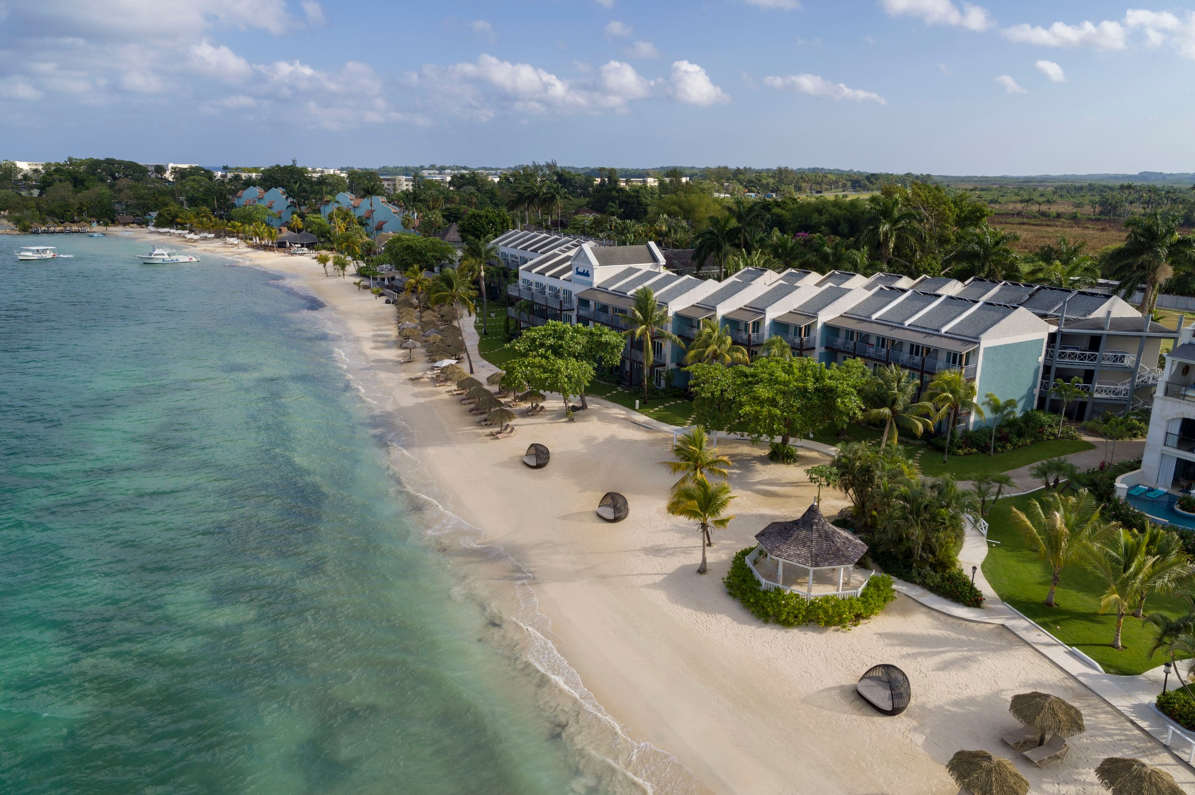 Aerial of the resort buildings, gardens and beach gazebo along the shoreline.