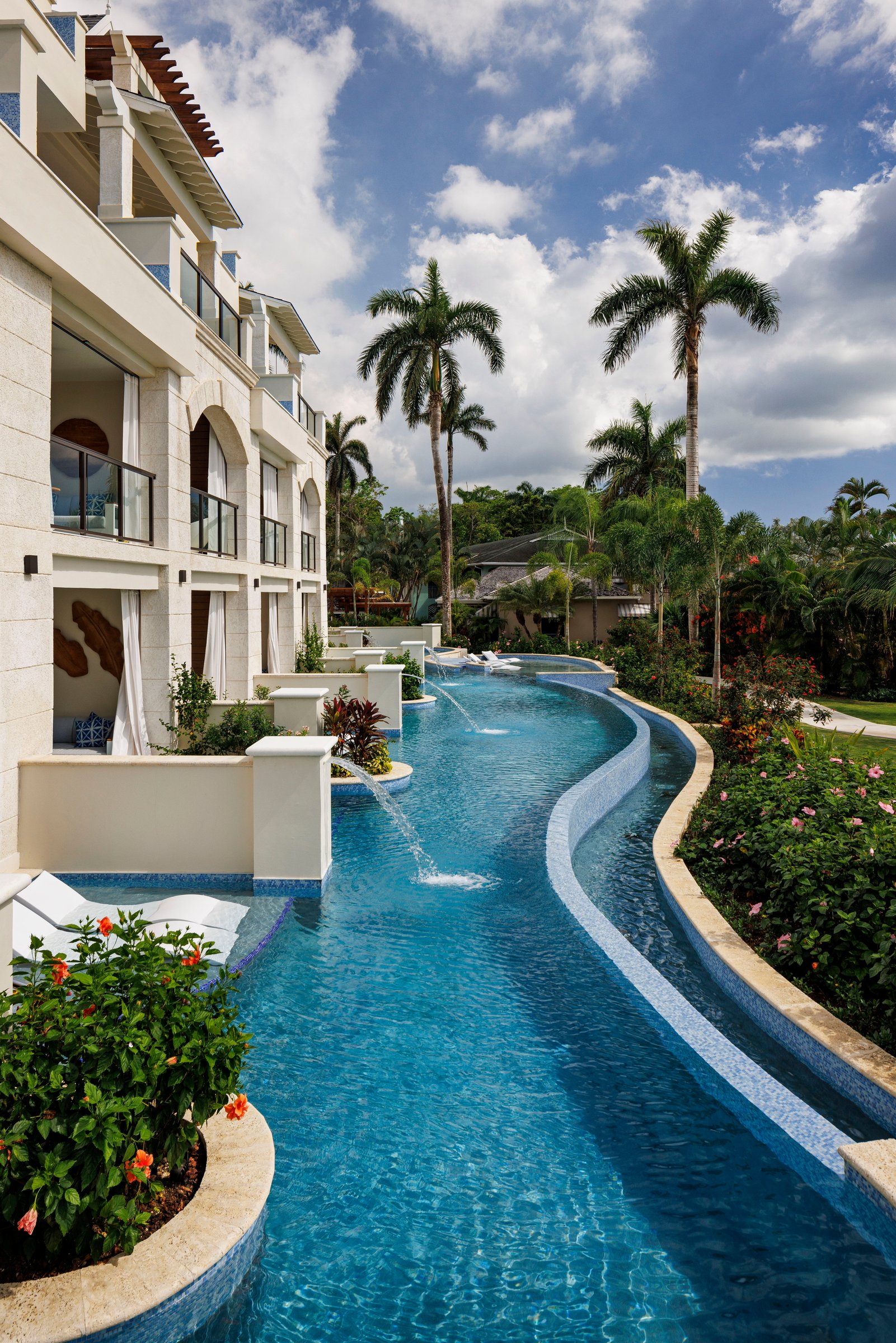 River pool running along the swim-up suite terraces under tall palms.