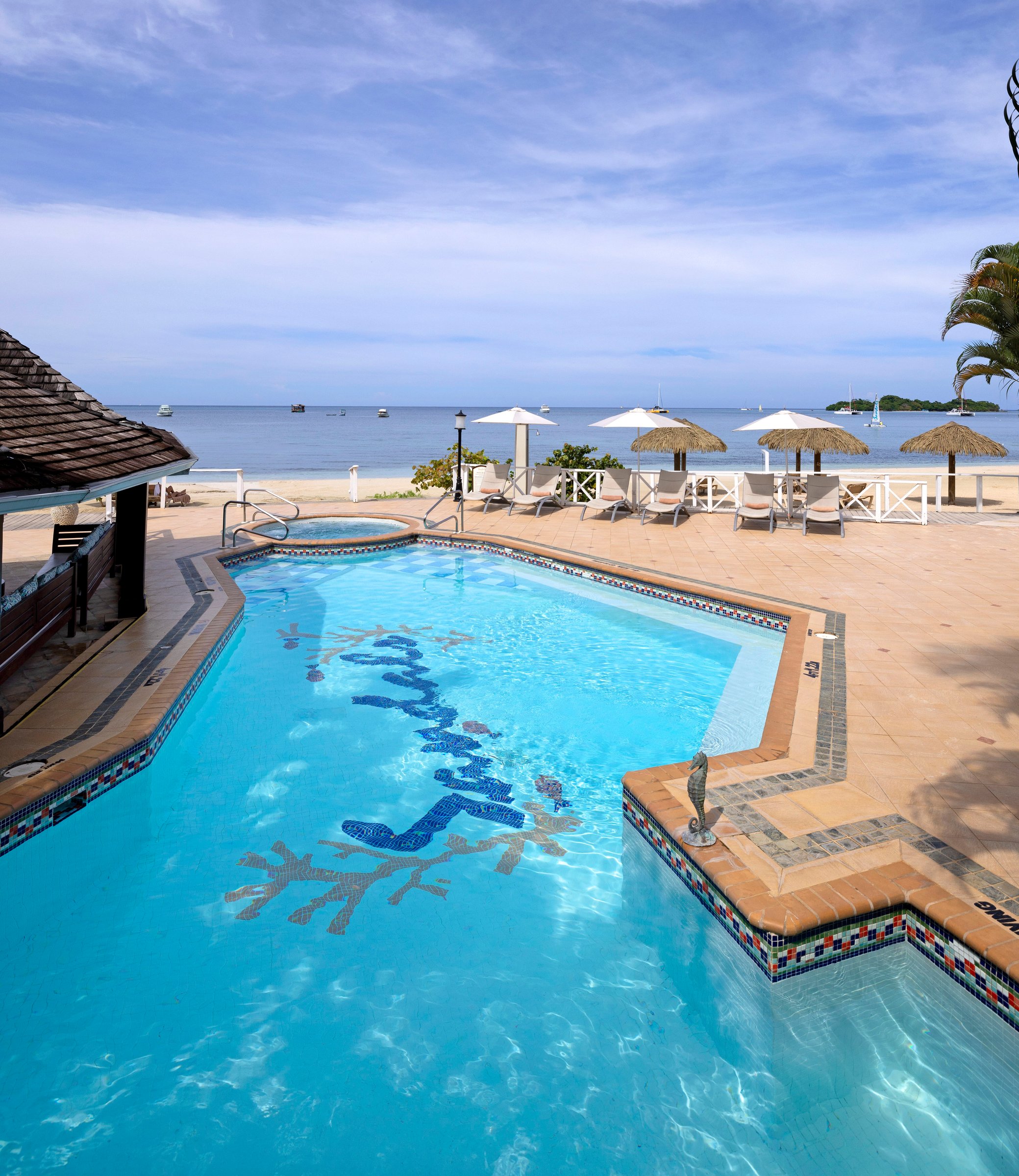 Mosaic pool beside the Piano Bar with umbrellas and the beach beyond.