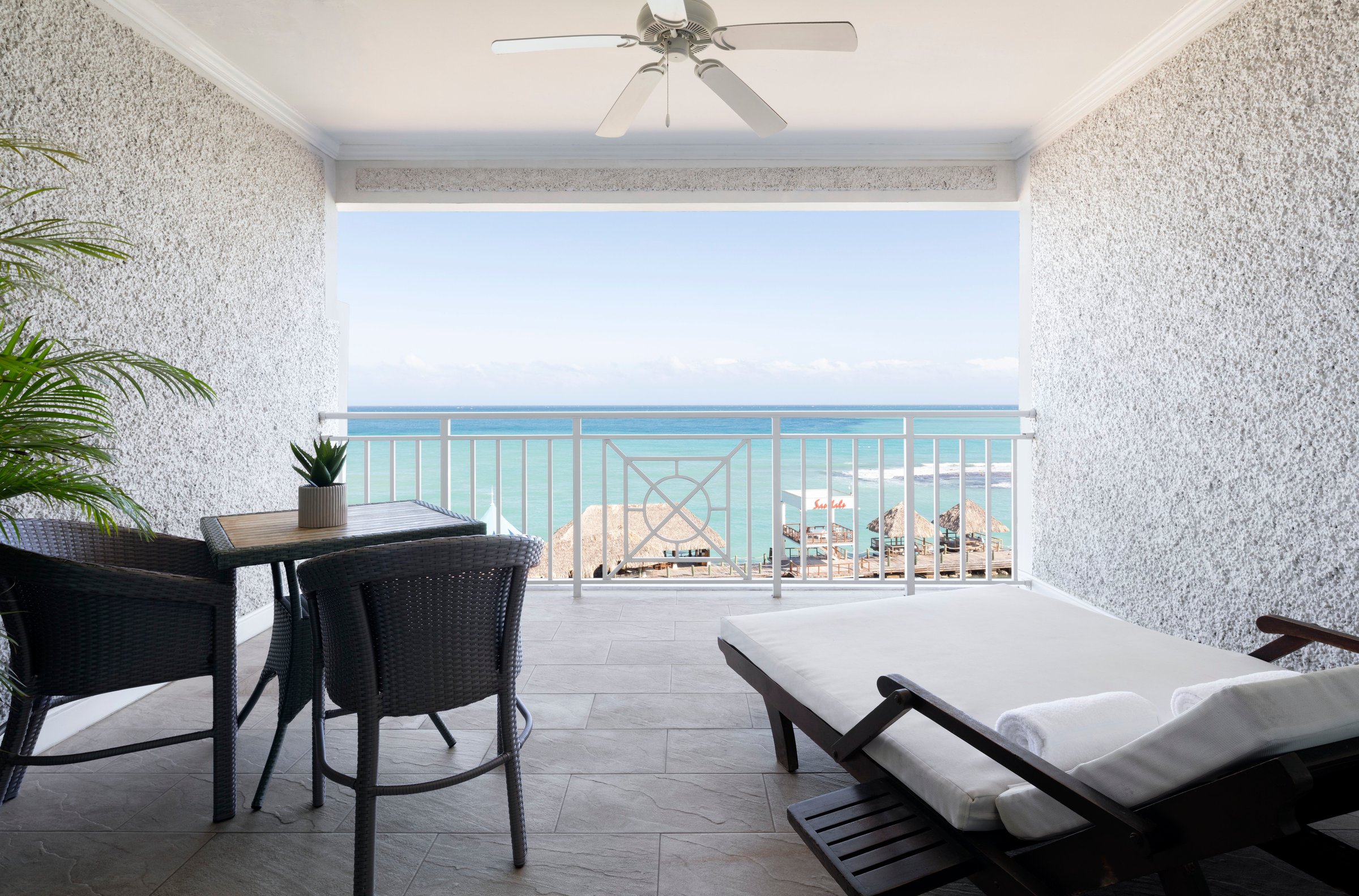 Covered balcony with a daybed and dining table facing the sea.
