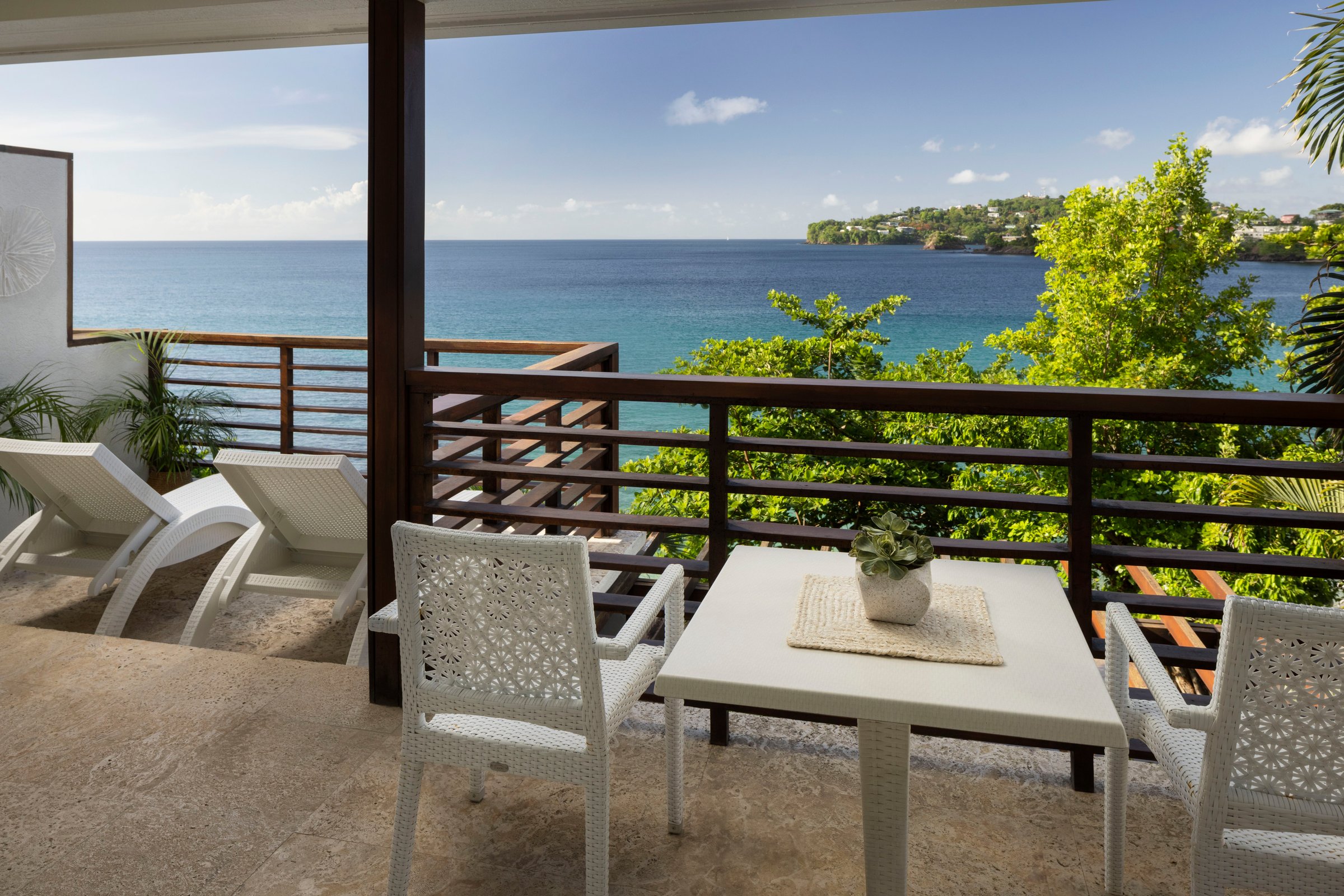 Suite balcony with a dining table and loungers overlooking the bay.