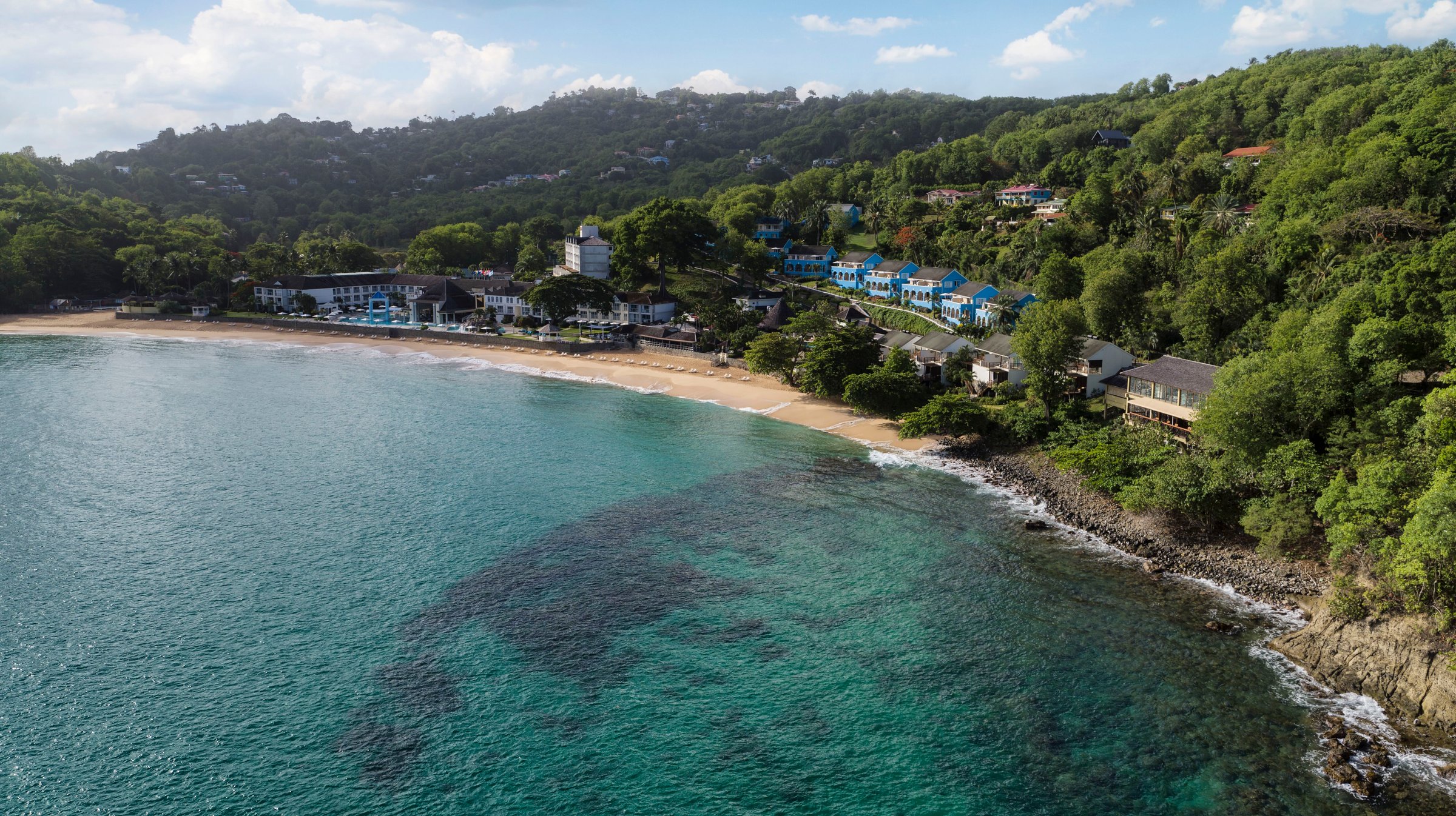 Aerial across the reef-dotted bay to the beach and hillside resort.