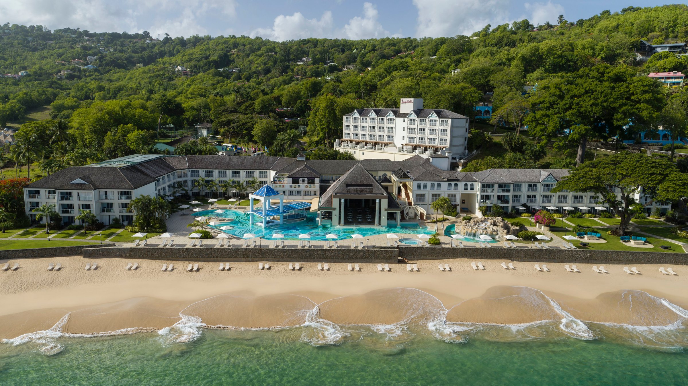 Frontal aerial of the main building, pools and beach.