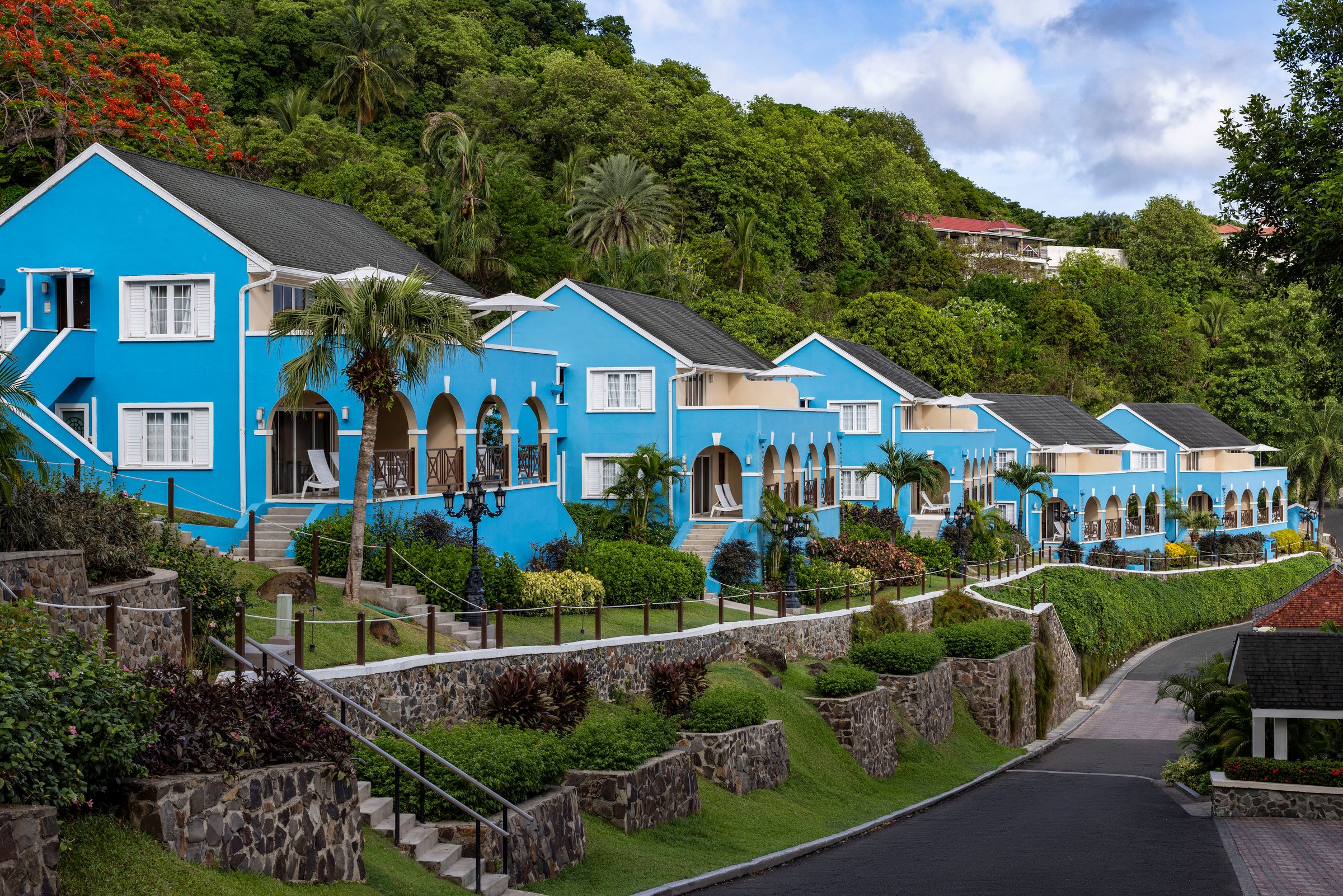 Row of blue hillside villa suites above terraced gardens.