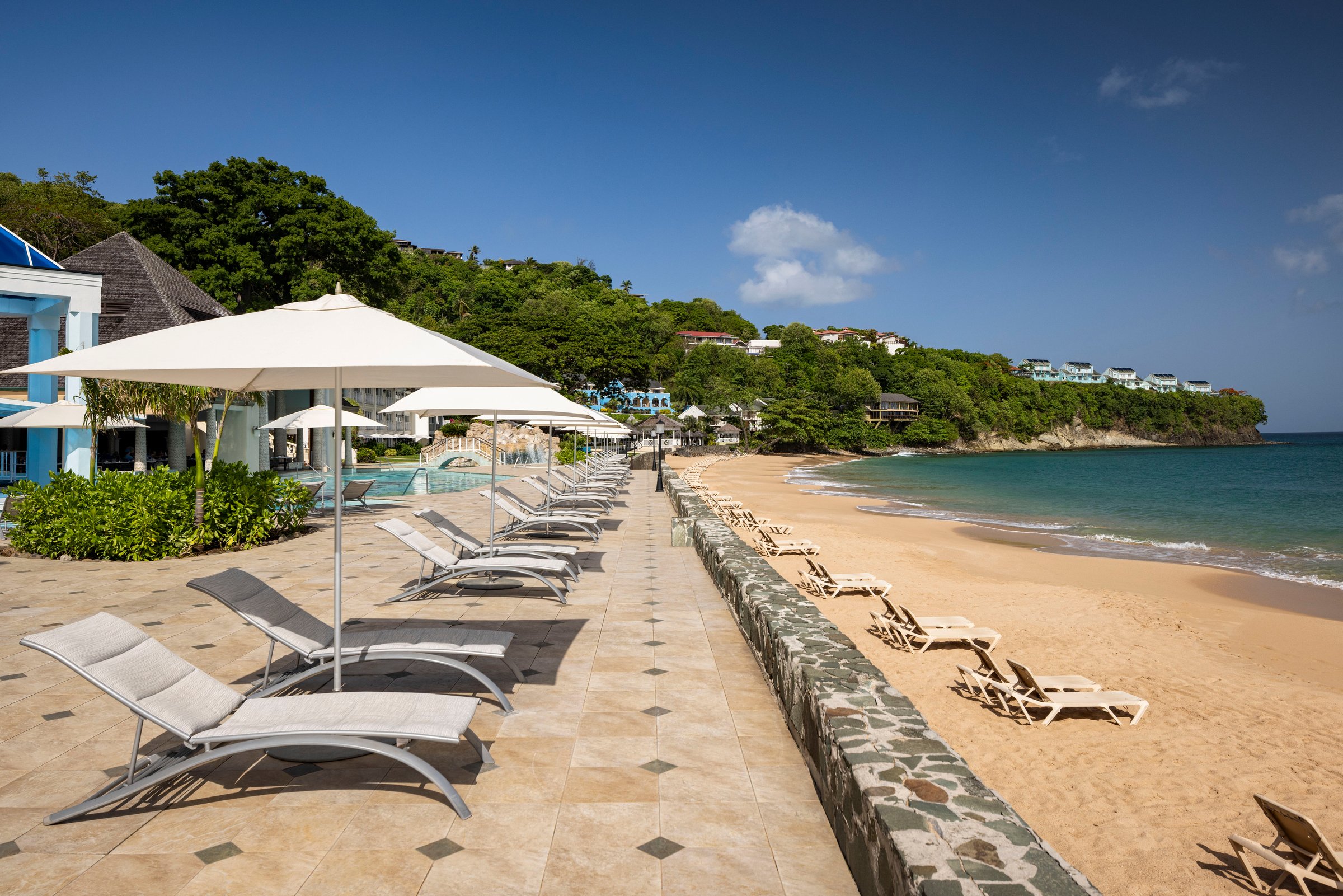 Beachfront pool deck with loungers and umbrellas along the seawall.
