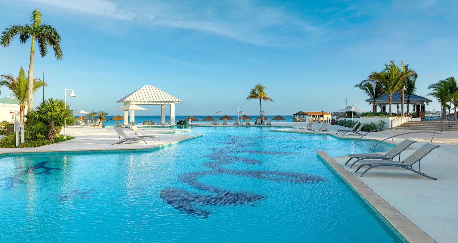 Large lagoon-style pool with lounge chairs facing the ocean, gazebo pavilion, and palm trees at Sandals Royal Bahamian.