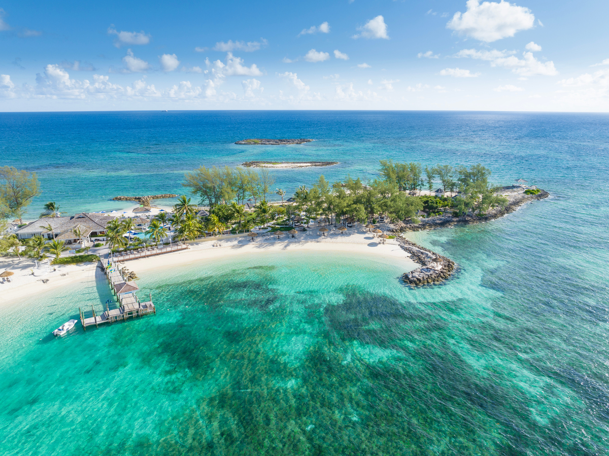Sandals Royal Bahamian beachfront with turquoise waters, white sand beach, palm trees, and a wooden dock with boat.