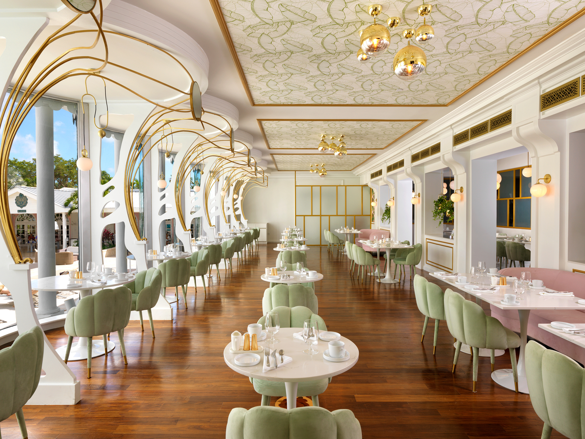 Elegant dining room with green velvet chairs, white round tables, gold curved archways, and patterned ceiling at Sandals Royal Bahamian.