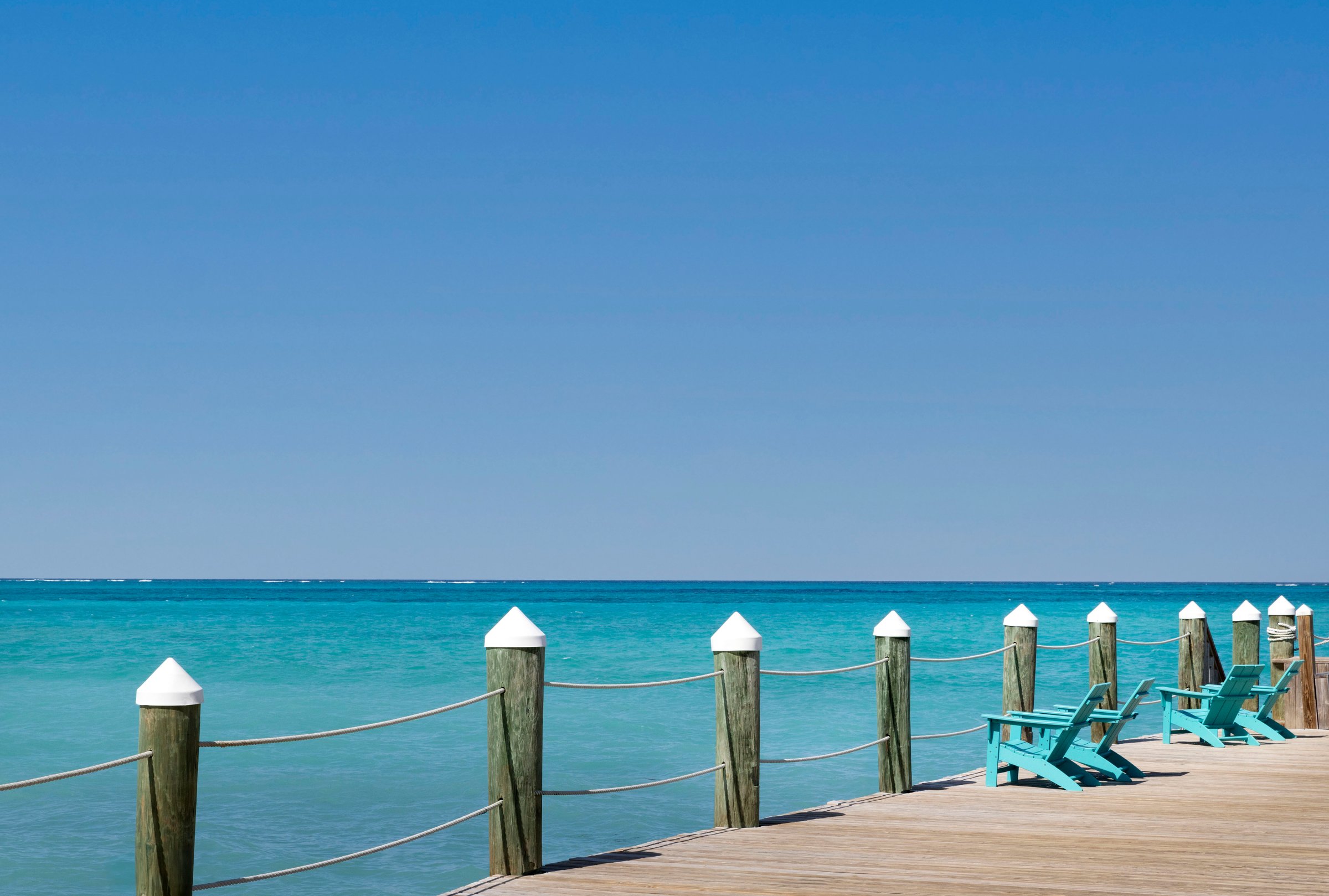 Pier with teal Adirondack chairs over clear turquoise water.