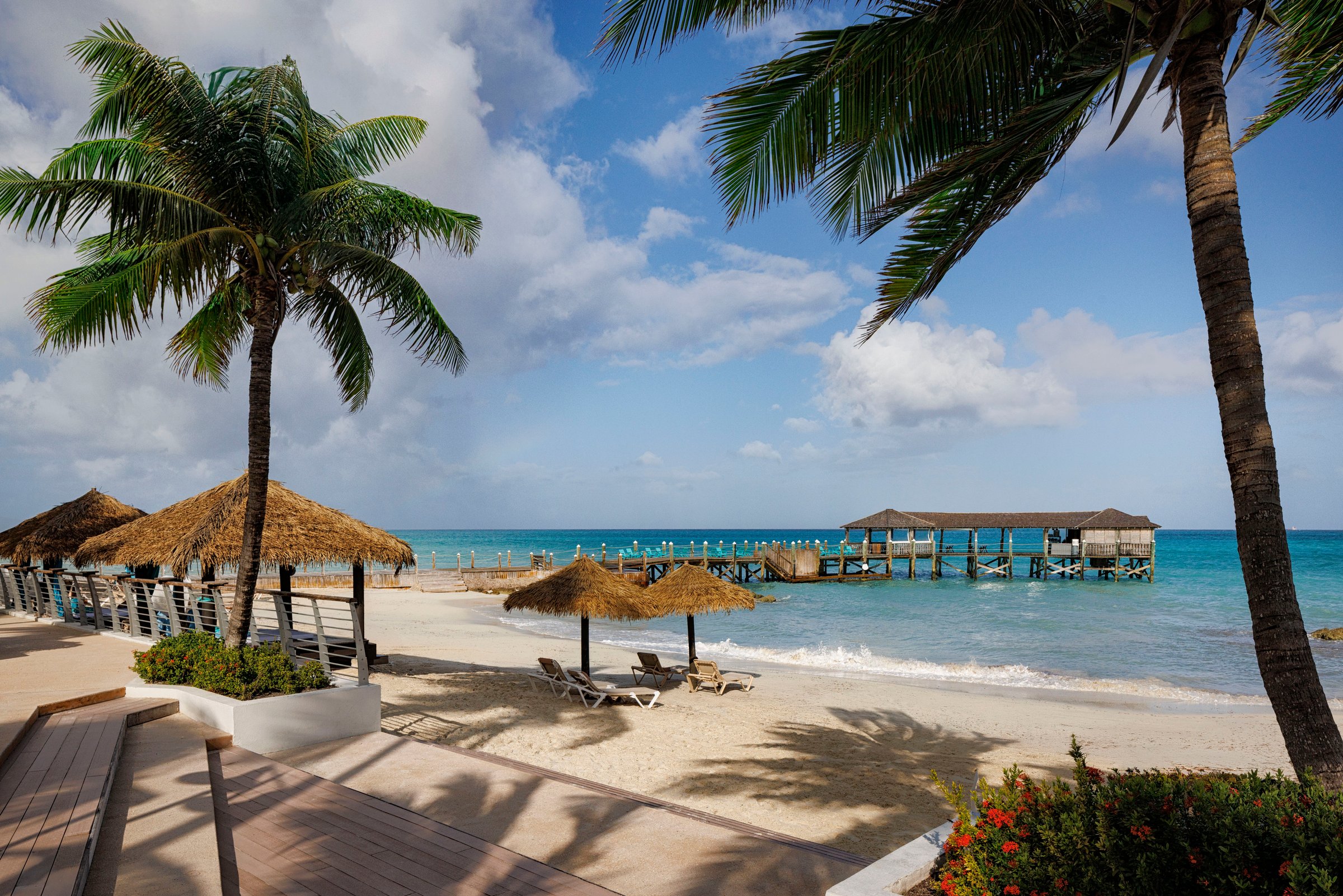 Beach with thatched umbrellas, palms and the overwater pier restaurant beyond.