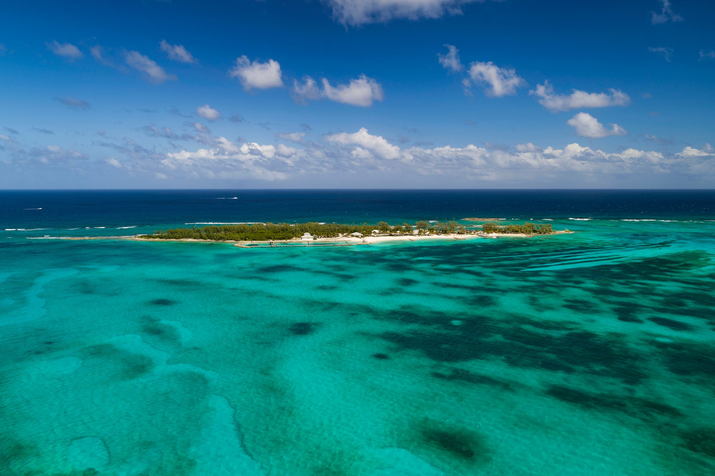 Aerial of the resort's private offshore island ringed by shallow turquoise reefs.