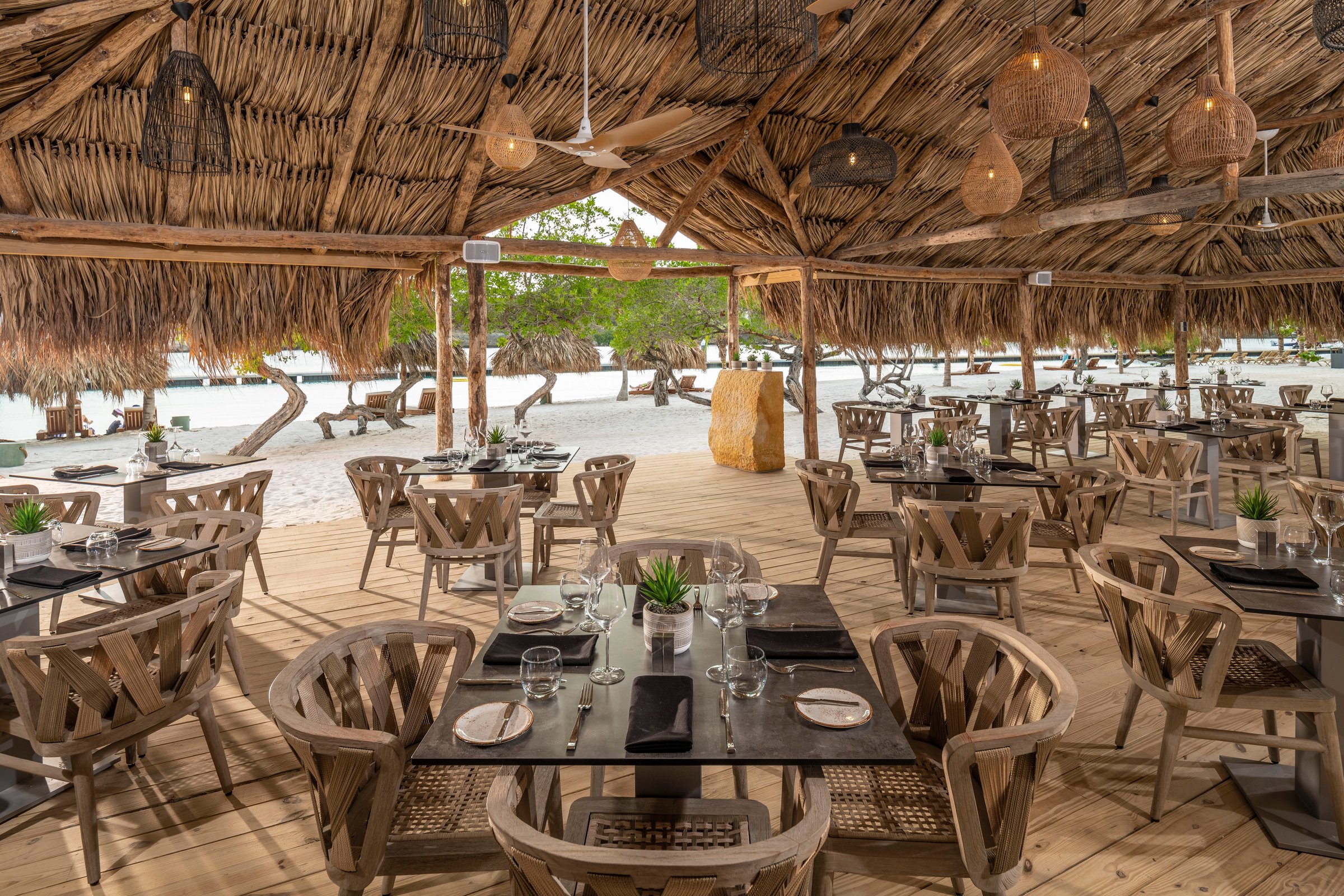 Thatched beachfront Strand restaurant with set tables.