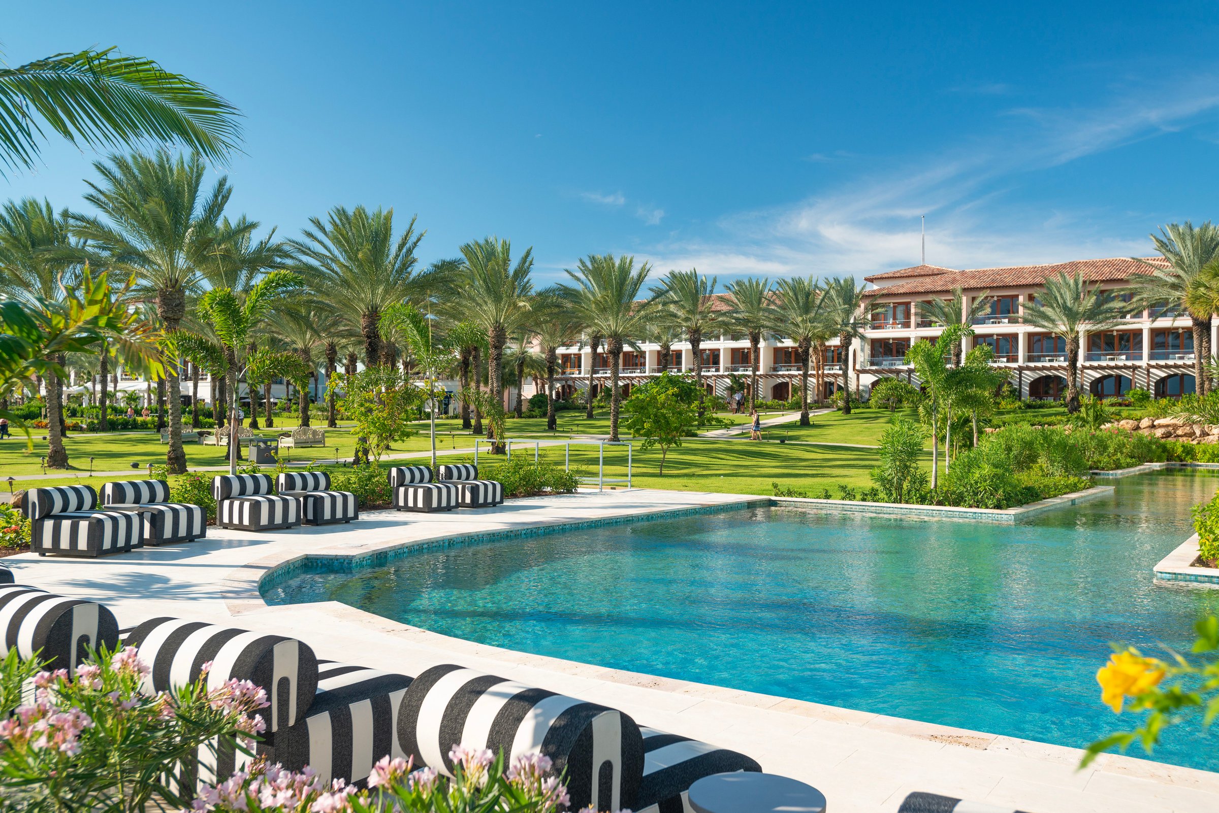 Pool with striped loungers and palm-lined lawns.