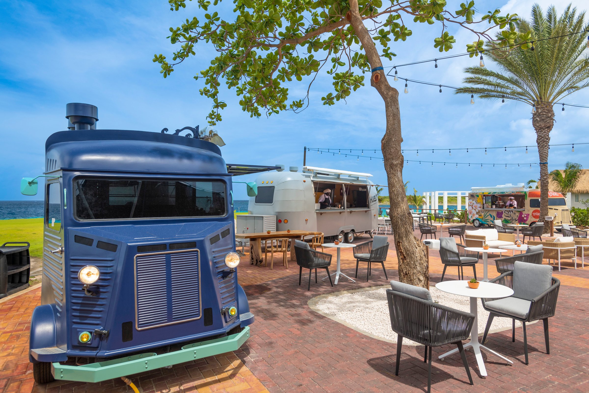 Vintage food trucks with patio tables by the sea.