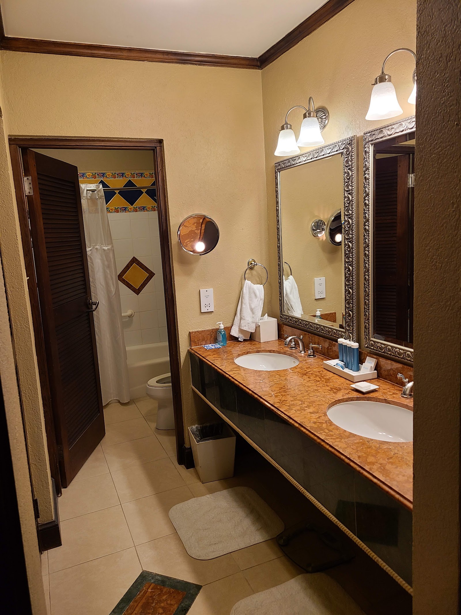 Resort bathroom with double vanity, decorative mirrors, sconces, and separate shower stall with yellow walls and dark wood trim.
