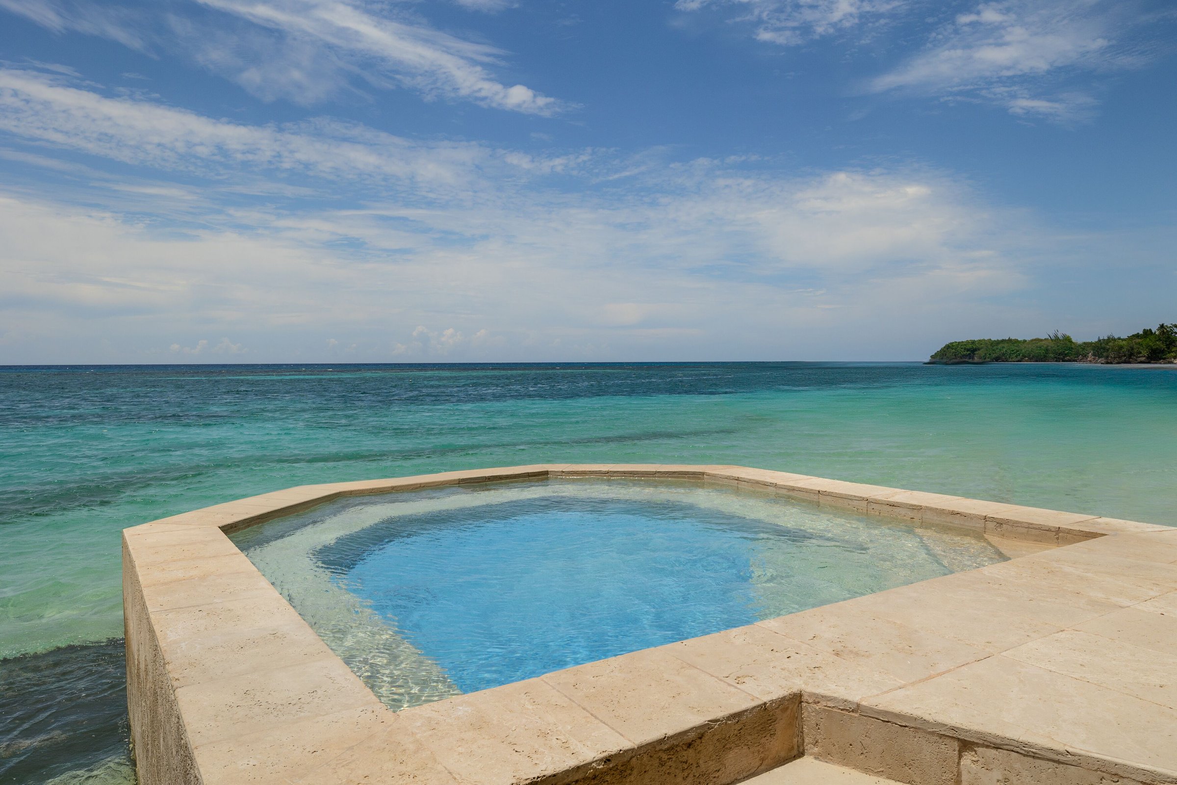 Stone-edged plunge pool at the water’s edge facing a green headland.