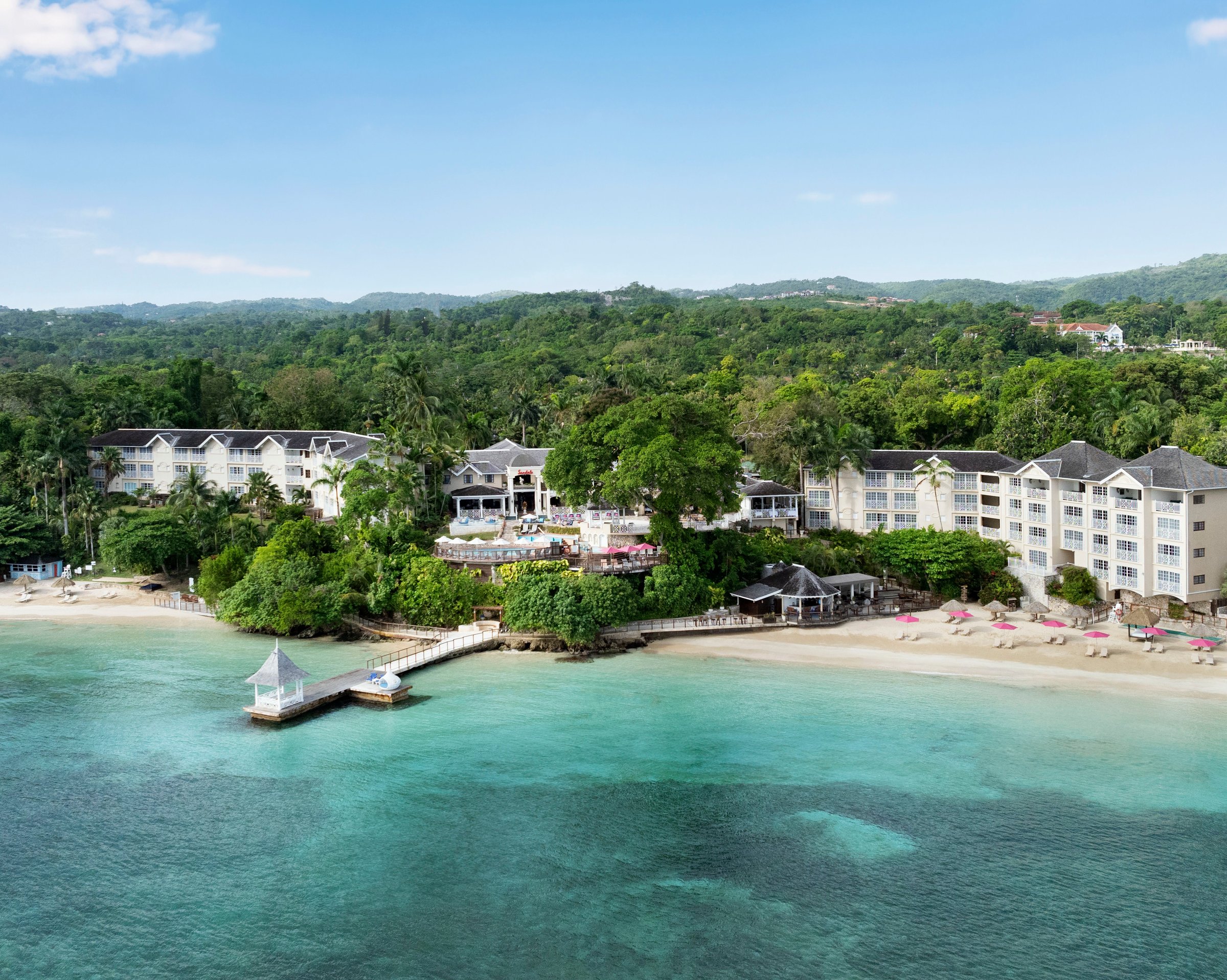 Aerial of the cliff-top plantation house, pier gazebo and turquoise cove.
