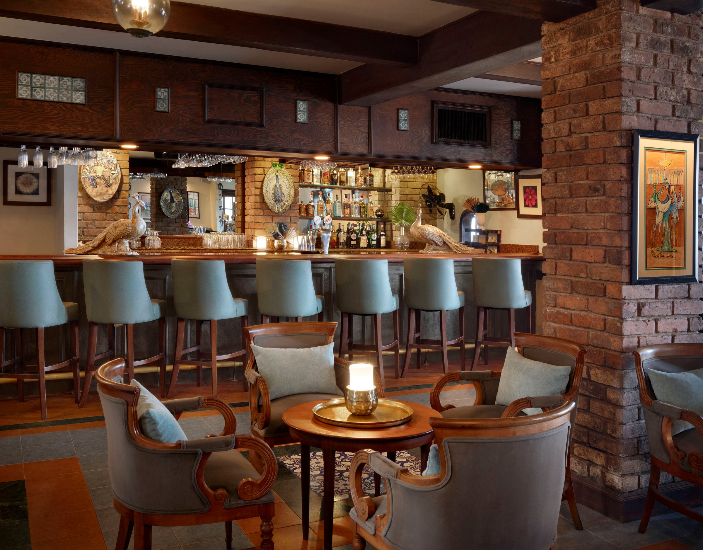 Wobbly Peacock pub bar with blue stools, brick pillar and leather armchairs.