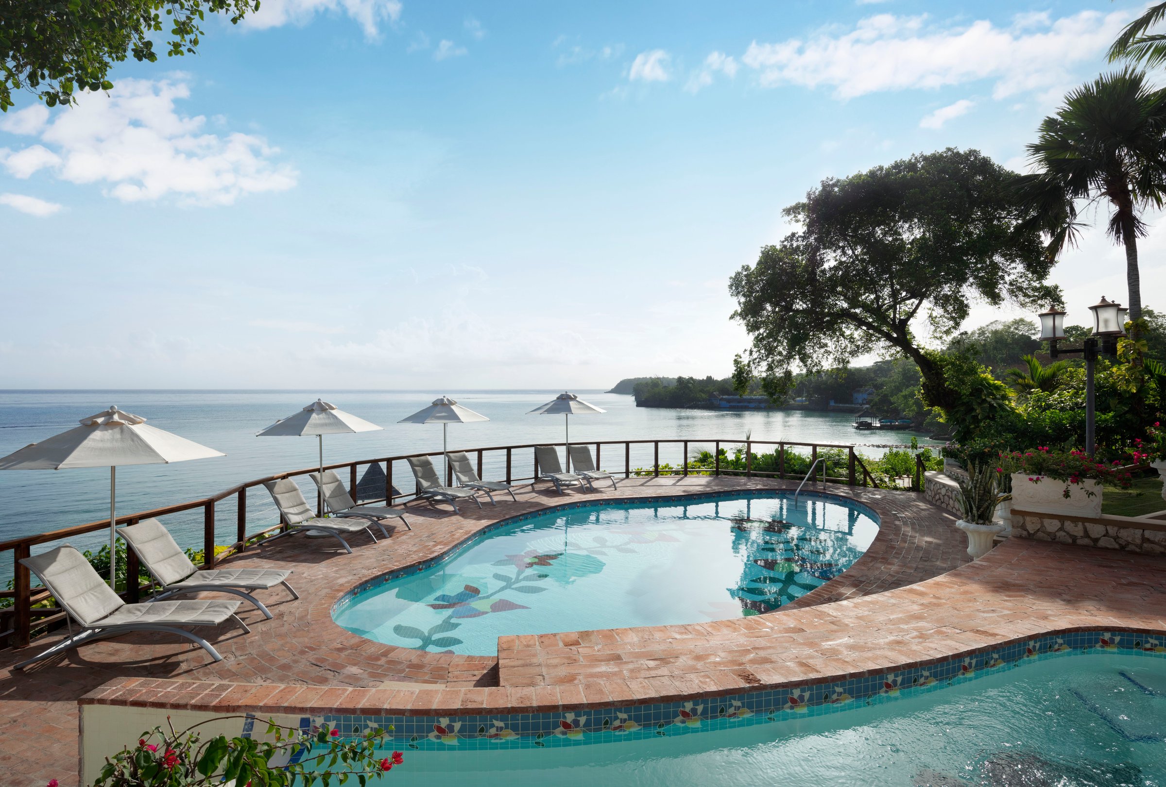 Clifftop pool with loungers and white umbrellas above the Caribbean.