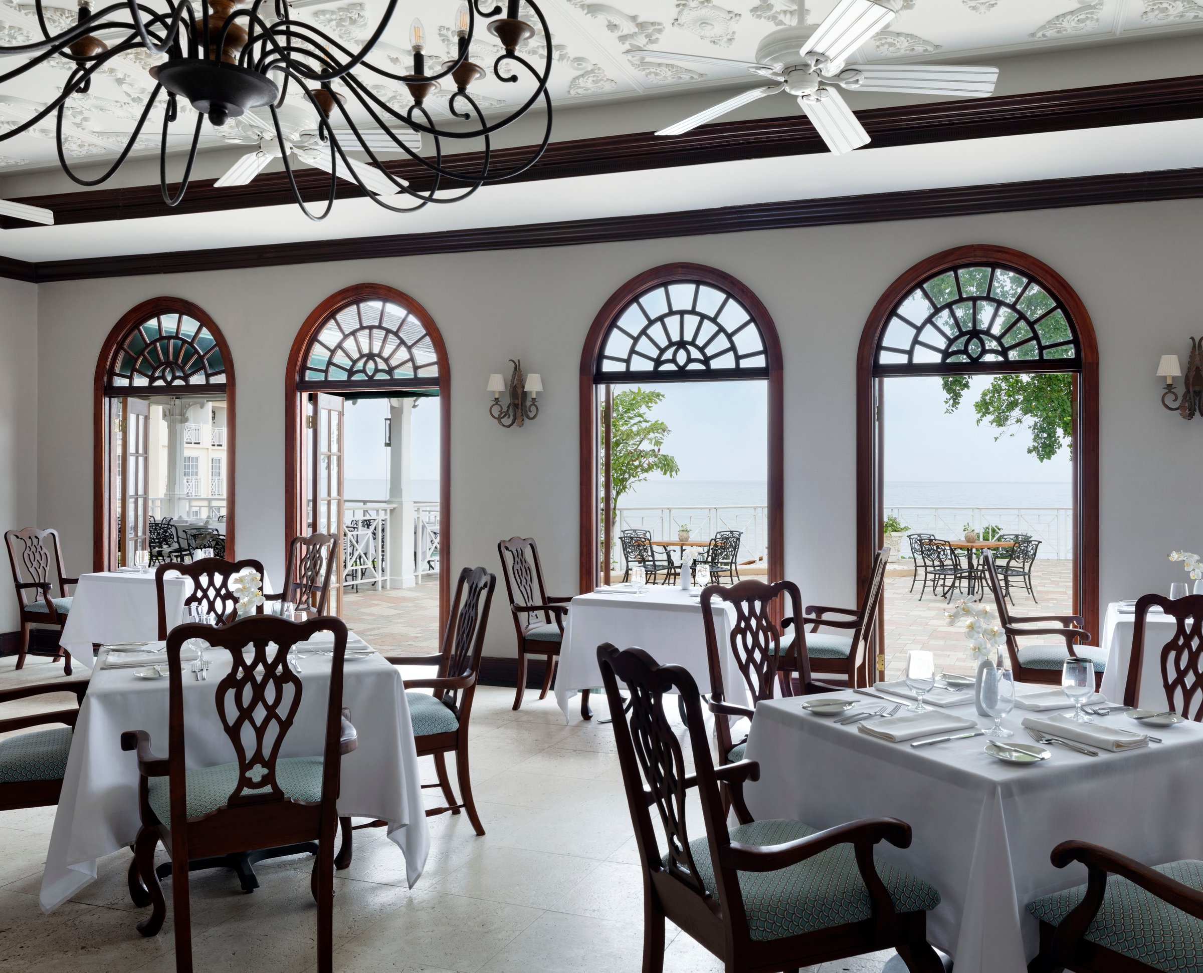 Terrace dining room with arched windows, chandeliers and white tablecloths.