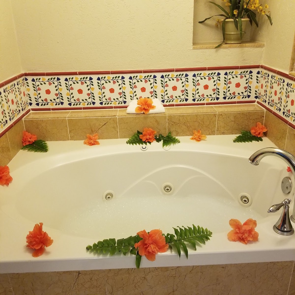 Whirlpool tub decorated with orange flowers and green fern fronds, surrounded by decorative tile with fruit and leaf patterns.