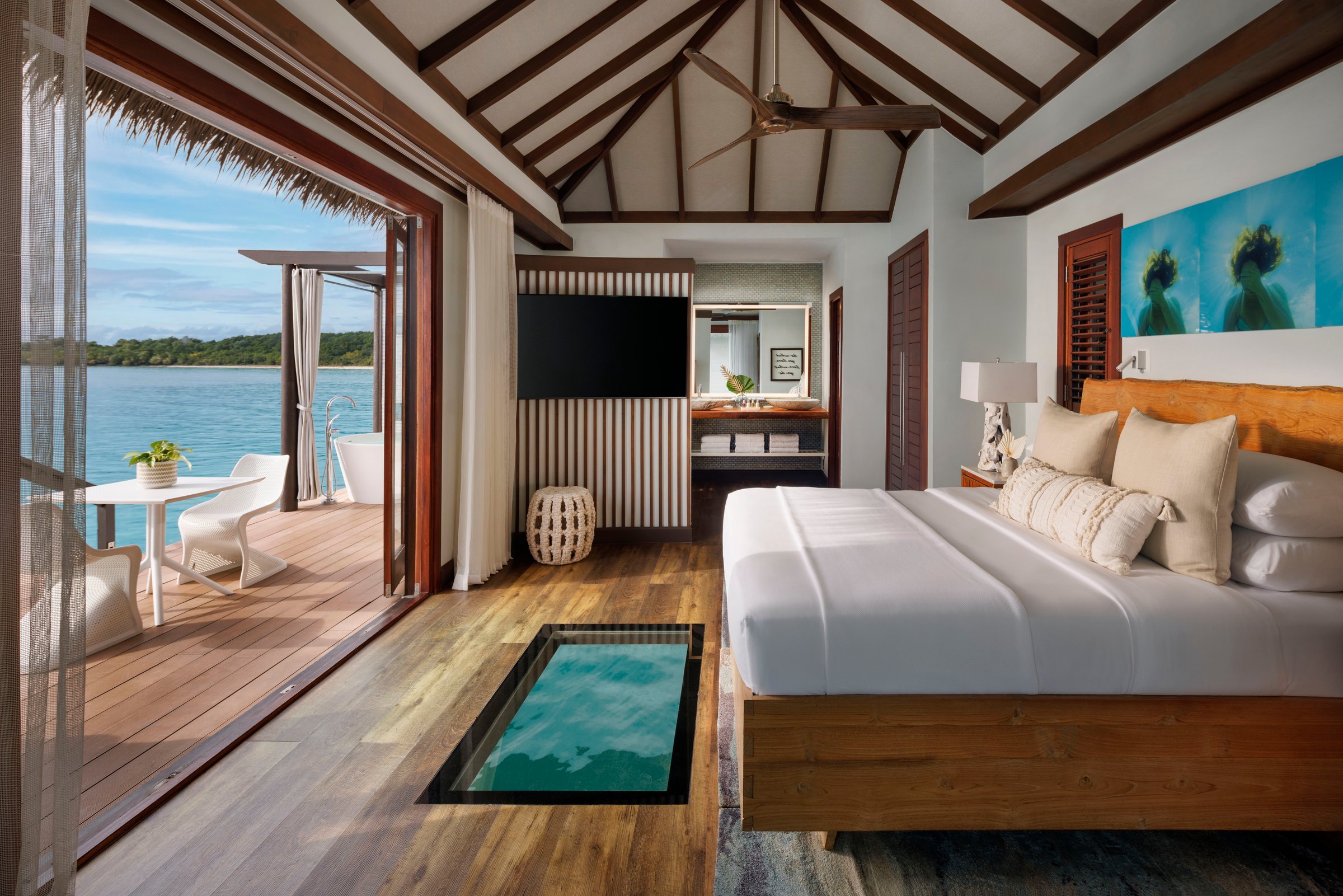 Over-water bungalow bedroom with a glass floor panel and sea deck.