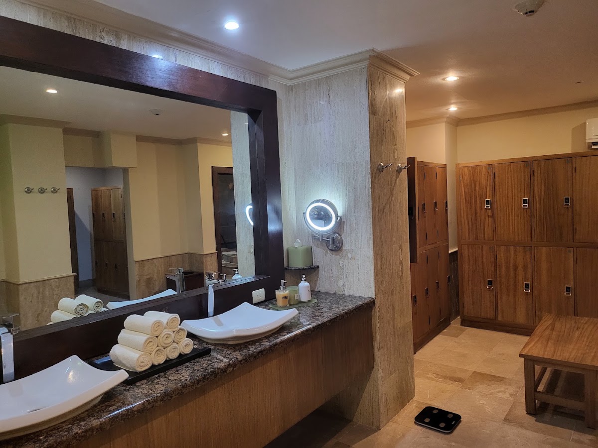 Spa bathroom with dual vanities, granite countertops, rolled white towels, illuminated mirror, and wooden lockers at Sandos Cancun.