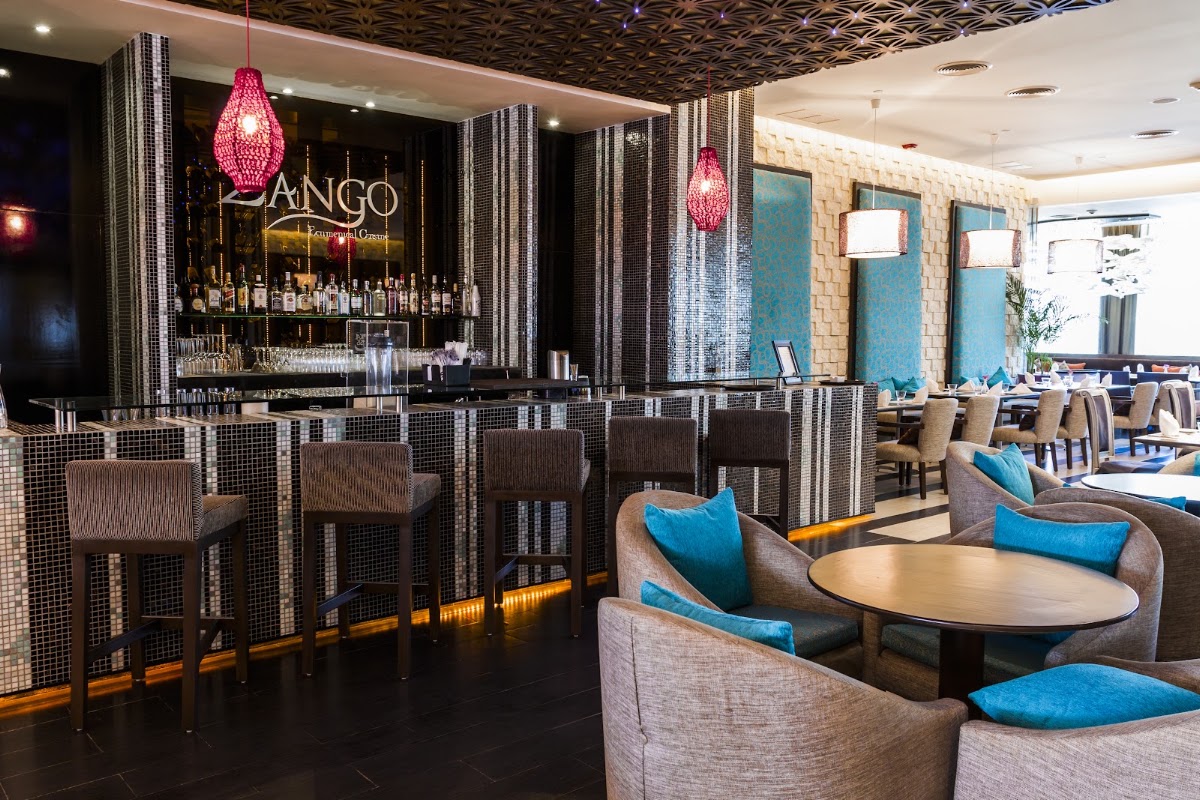 Tango bar at Sandos Cancun with gray upholstered seating, blue accent pillows, pink beaded pendant lights, and black tile accents.