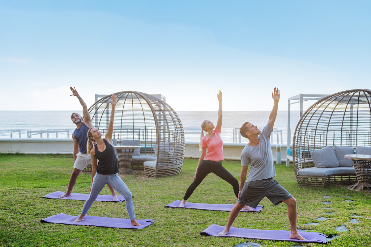 Group doing yoga on grass near the beach with woven pod chairs and ocean view at Sandos Cancun.