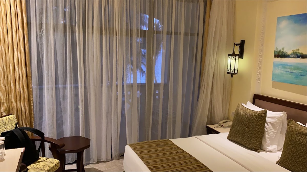 Guest room at Sarova Whitesands Beach Resort with queen bed, sheer curtains, and ocean view from balcony.