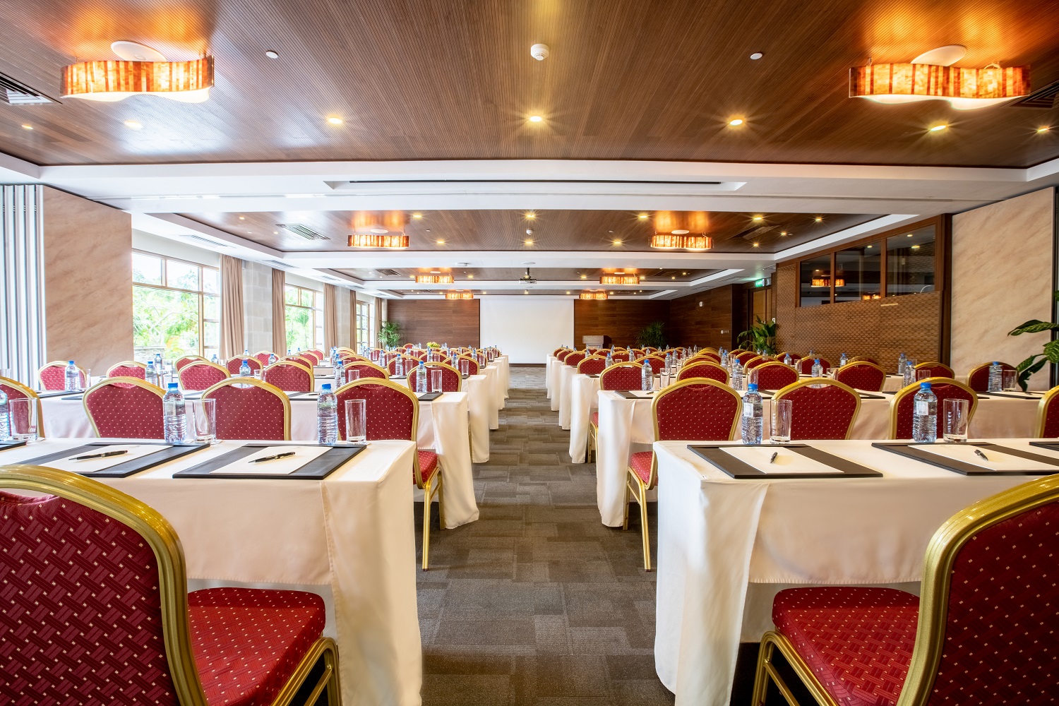 Conference room with rows of tables draped in cream linens, red and gold chairs, recessed lighting, and large windows at Savoy Seychelles Resort & Spa.