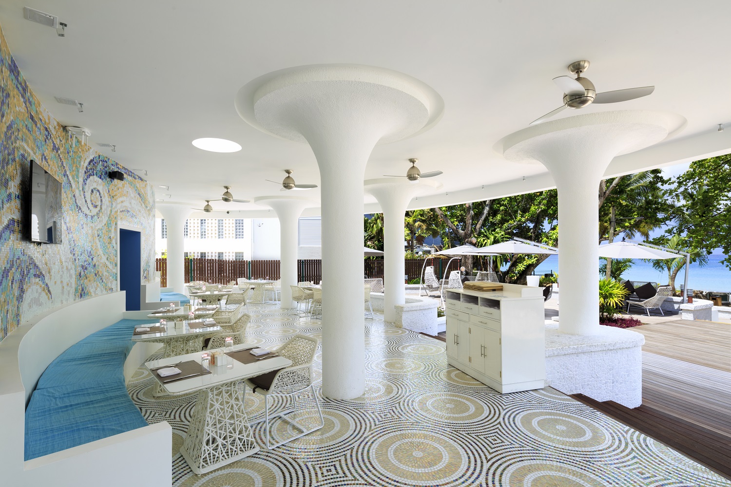 Modern dining area at Savoy Seychelles with curved columns, geometric floor tiles, and ocean views through open archways.