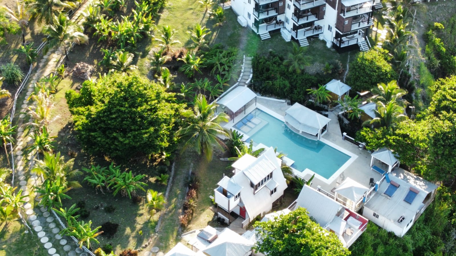 Aerial view of Sea Cliff Resort & Spa with turquoise pool, white cabanas, guest buildings, and lush tropical vegetation surrounding the property.