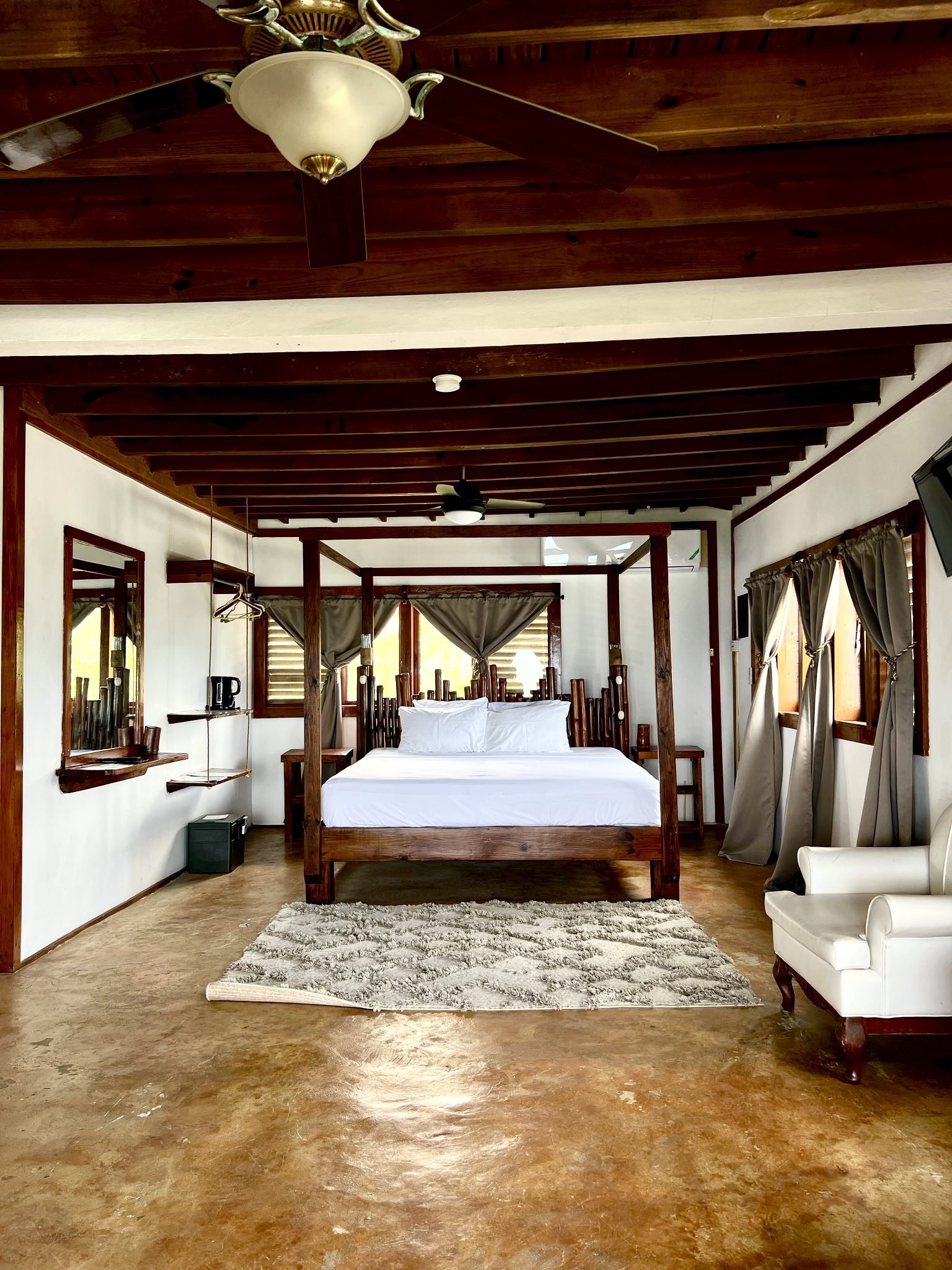 Spacious bedroom with dark wood four-poster bed, white bedding, polished concrete floors, and wooden beam ceiling at Sea Cliff Resort & Spa.
