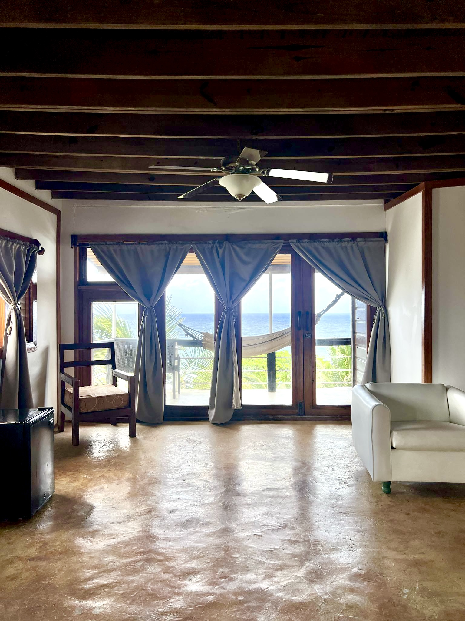 Sea Cliff Resort & Spa suite interior with blue curtains, concrete floor, and ocean view through glass doors.