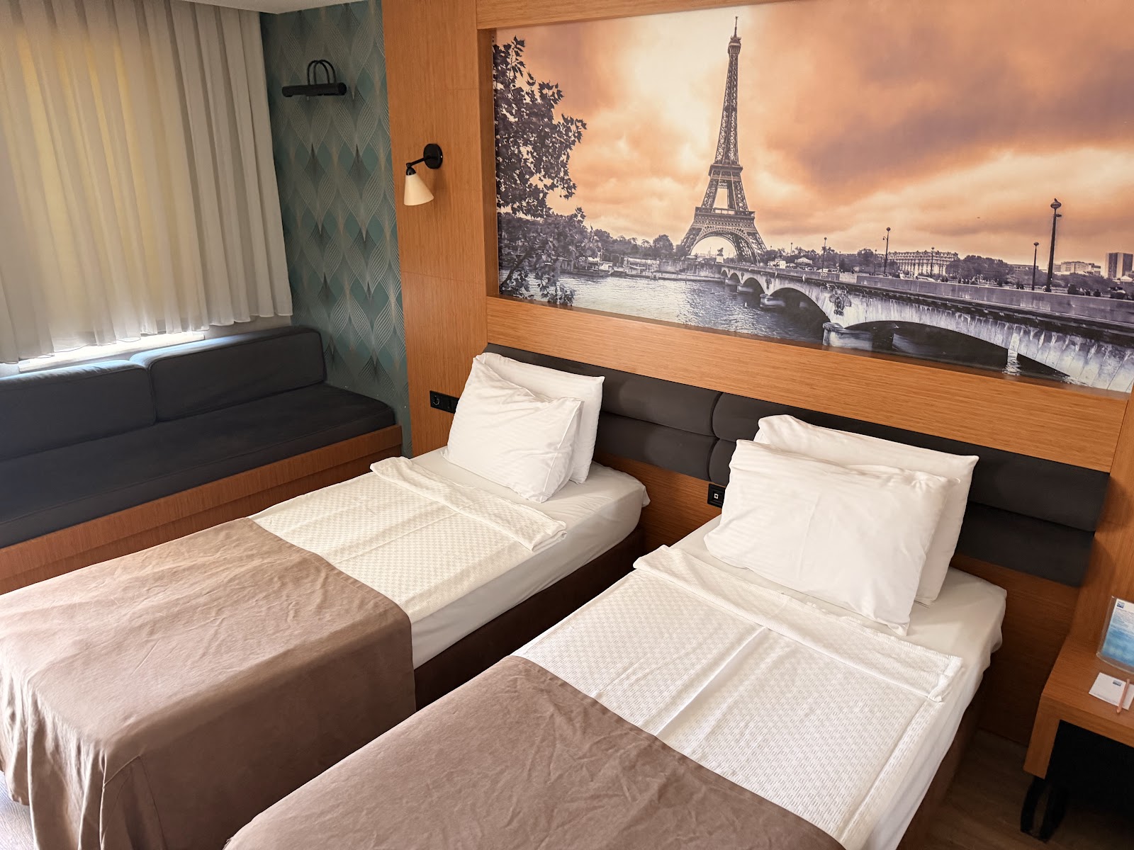 Modern resort suite with teal seating area, queen beds, and adjoining room visible through open doorway.