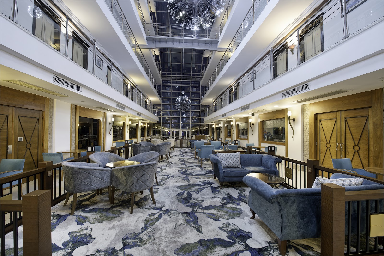 Modern atrium lobby with blue seating areas, decorative chandelier, and patterned flooring in the Sealife Family Resort Hotel.